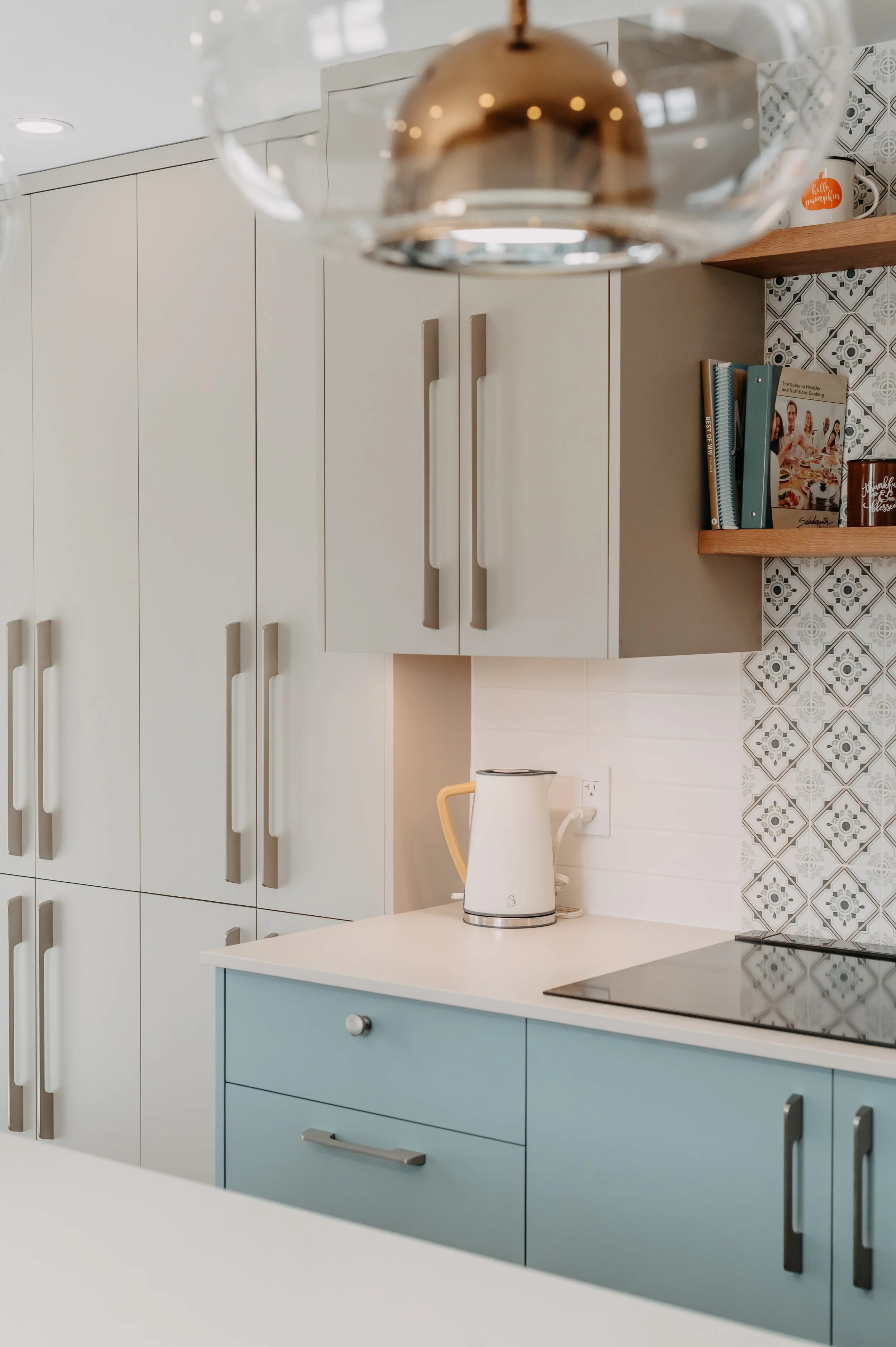 Soft, light-toned upper cabinets and a patterned tile backsplash tie the kitchen's blue and neutral palette together