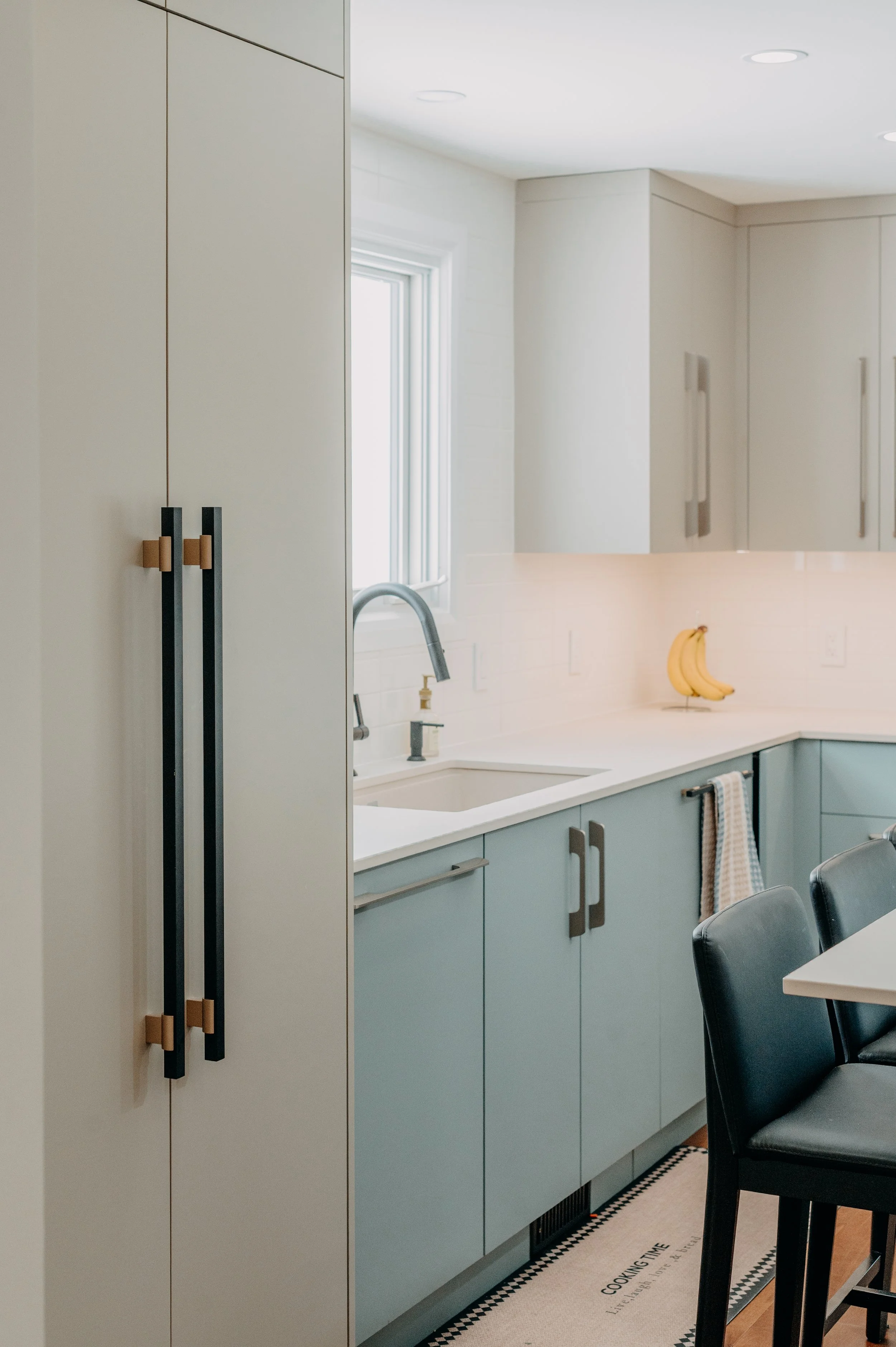 Slim champagne and black hardware paired with a sleek faucet, adding a refined finishing touch to the blue lower cabinets.