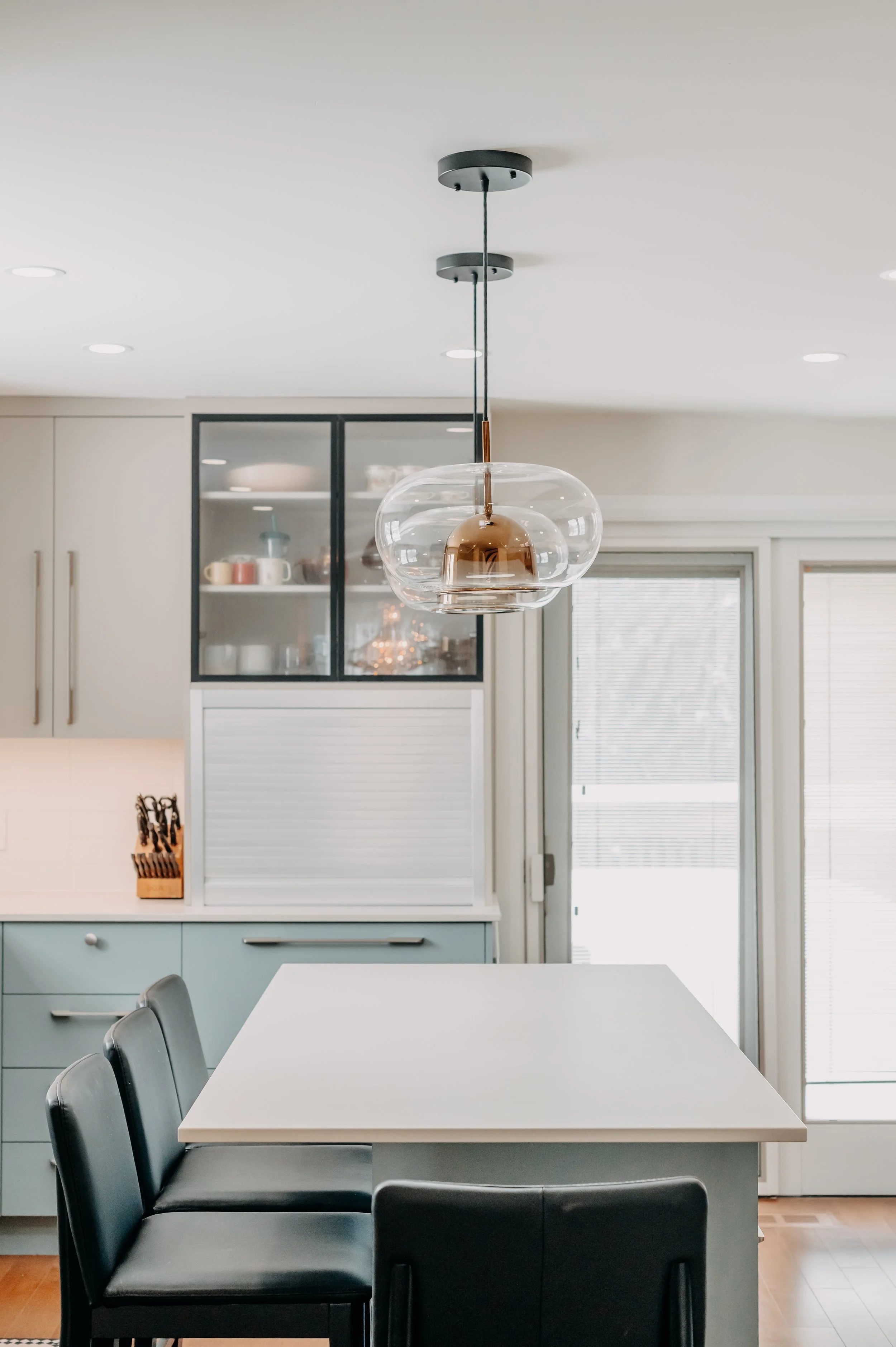 A glass-front upper cabinet and warm brass pendant light bring elegance above the kitchen's blue lower cabinetry.
