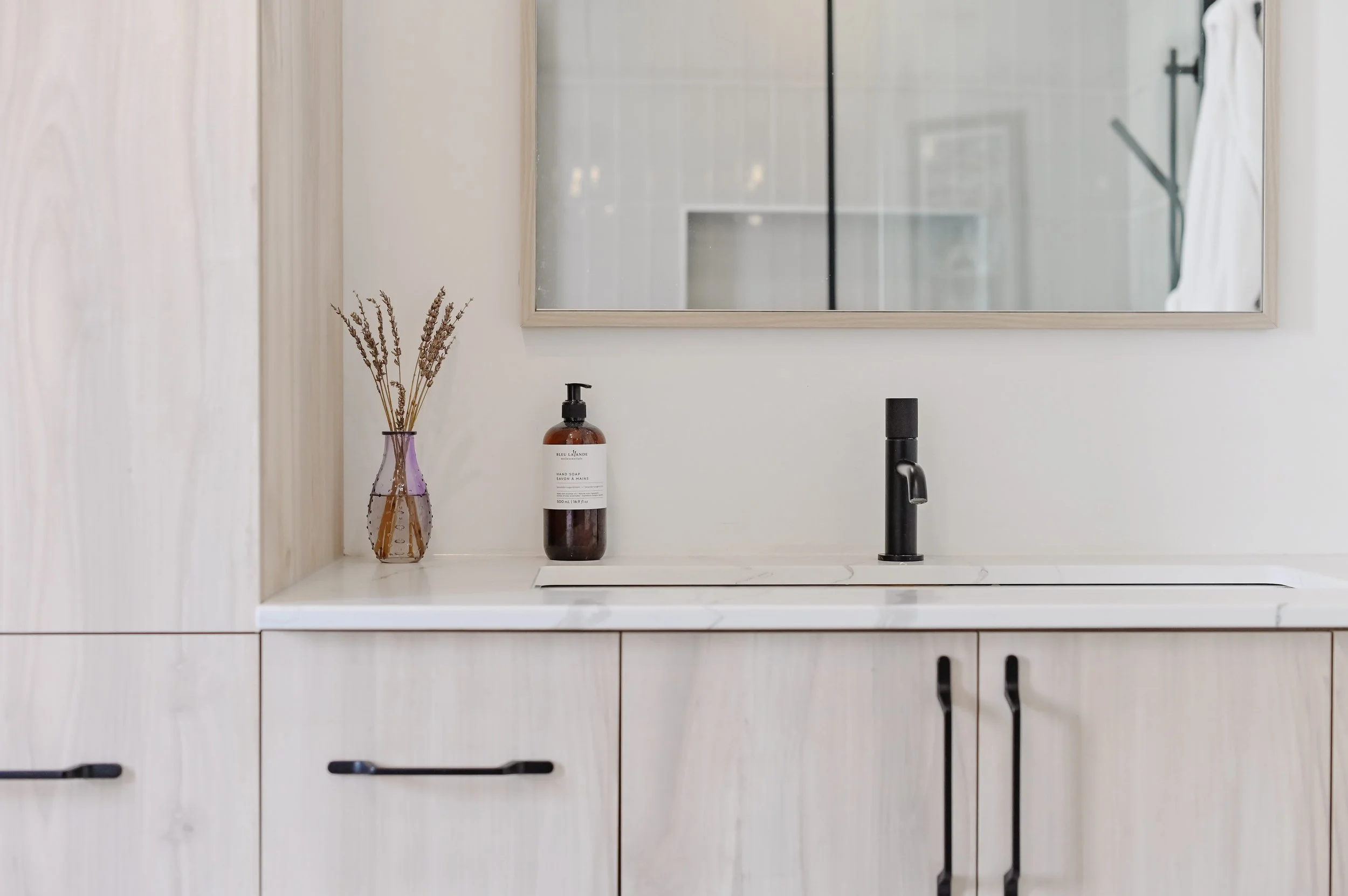 New York style bathroom vanity with black faucet, dried lavender décor, and mirror reflecting the glass shower, Montreal West