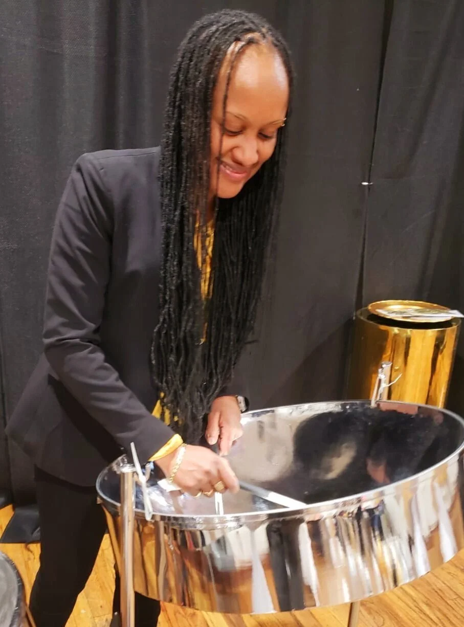 Woman with long braids playing a polished steel pan drum on stage