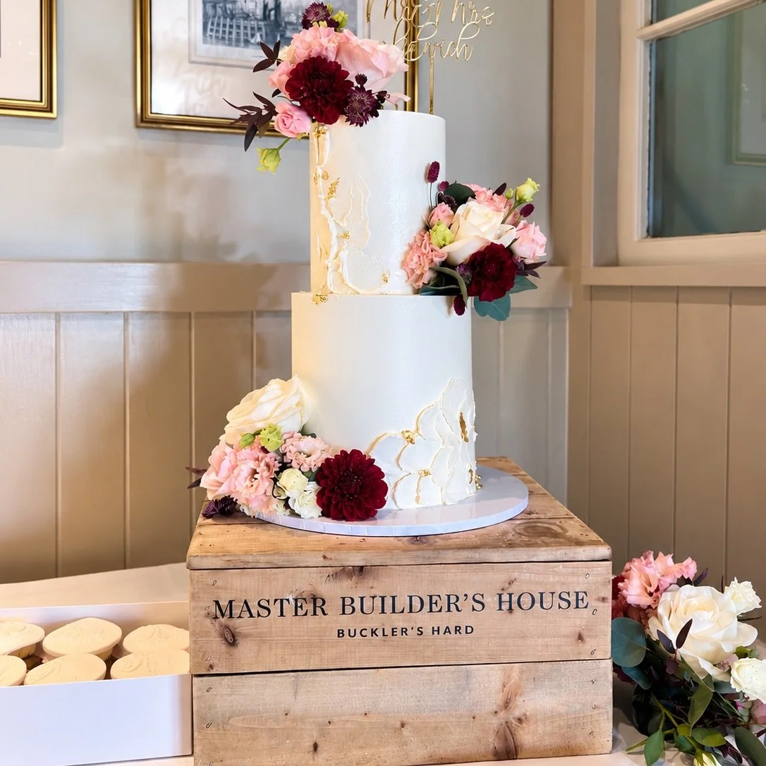 A beautiful two-tier wedding cake created for our lovely couple at The Master Builder&rsquo;s House, Buckler&rsquo;s Hard.

Finished in white chocolate ganache with textured floral details, gold accents and beautiful flowers.

Even more special was r