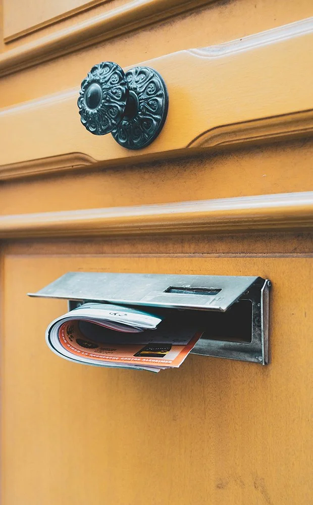 A mailbox with a black decorative door handle above it, mounted on a wooden door or wall.