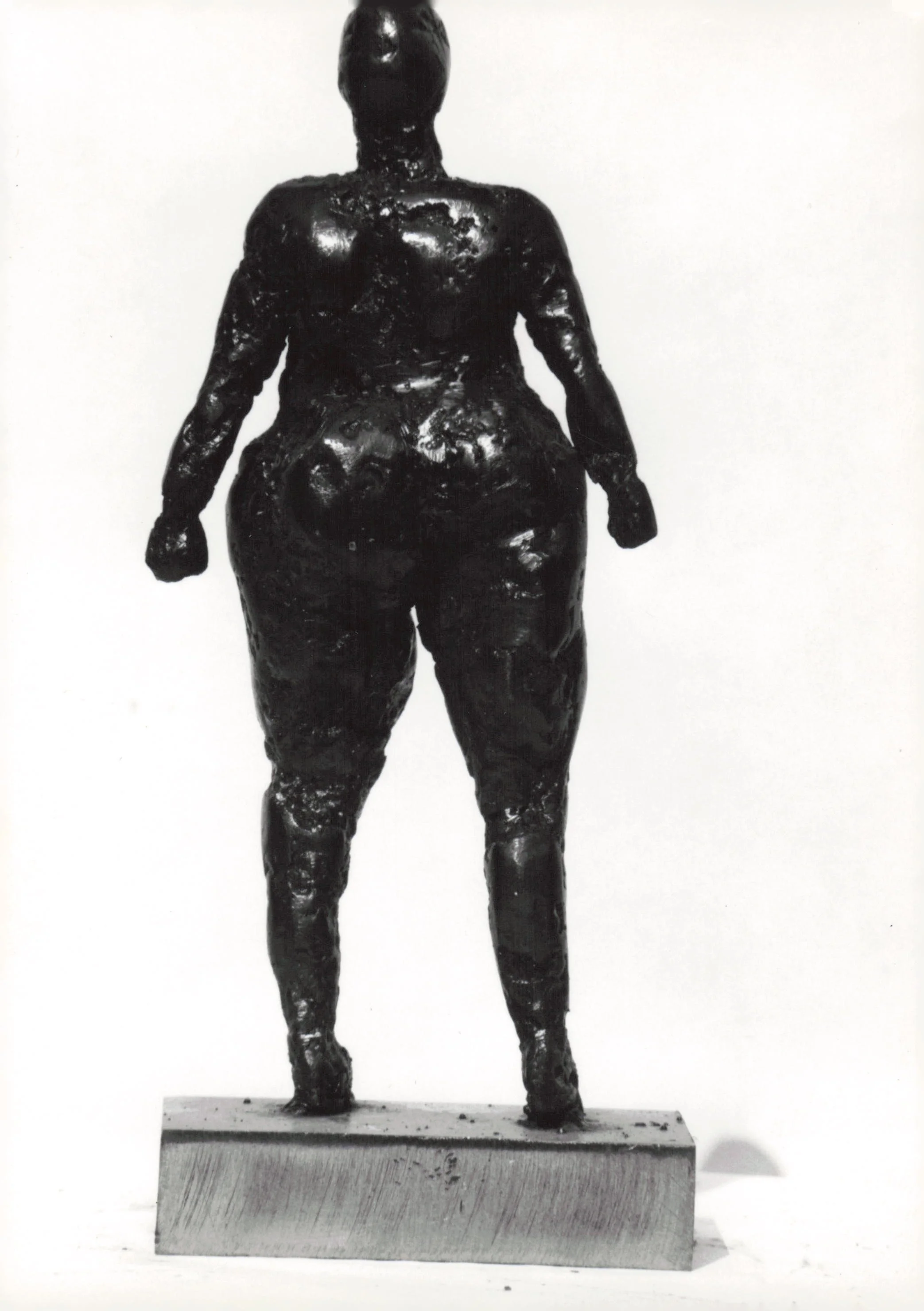 Black sculpture of a human figure standing on a pedestal against a plain white background.
