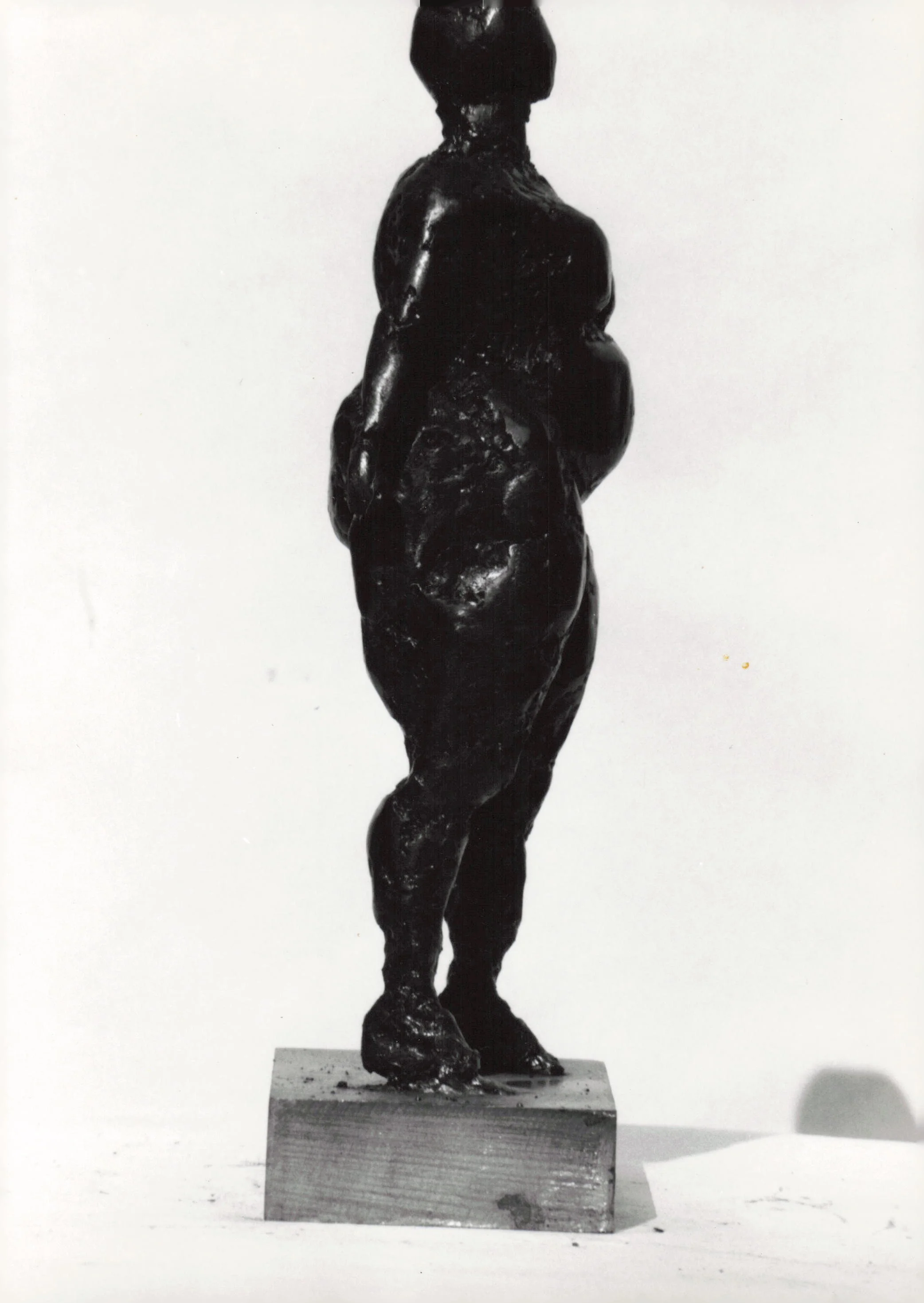 A black statue of a human figure standing on a rectangular base, with its back to the viewer, in a minimalist setting.