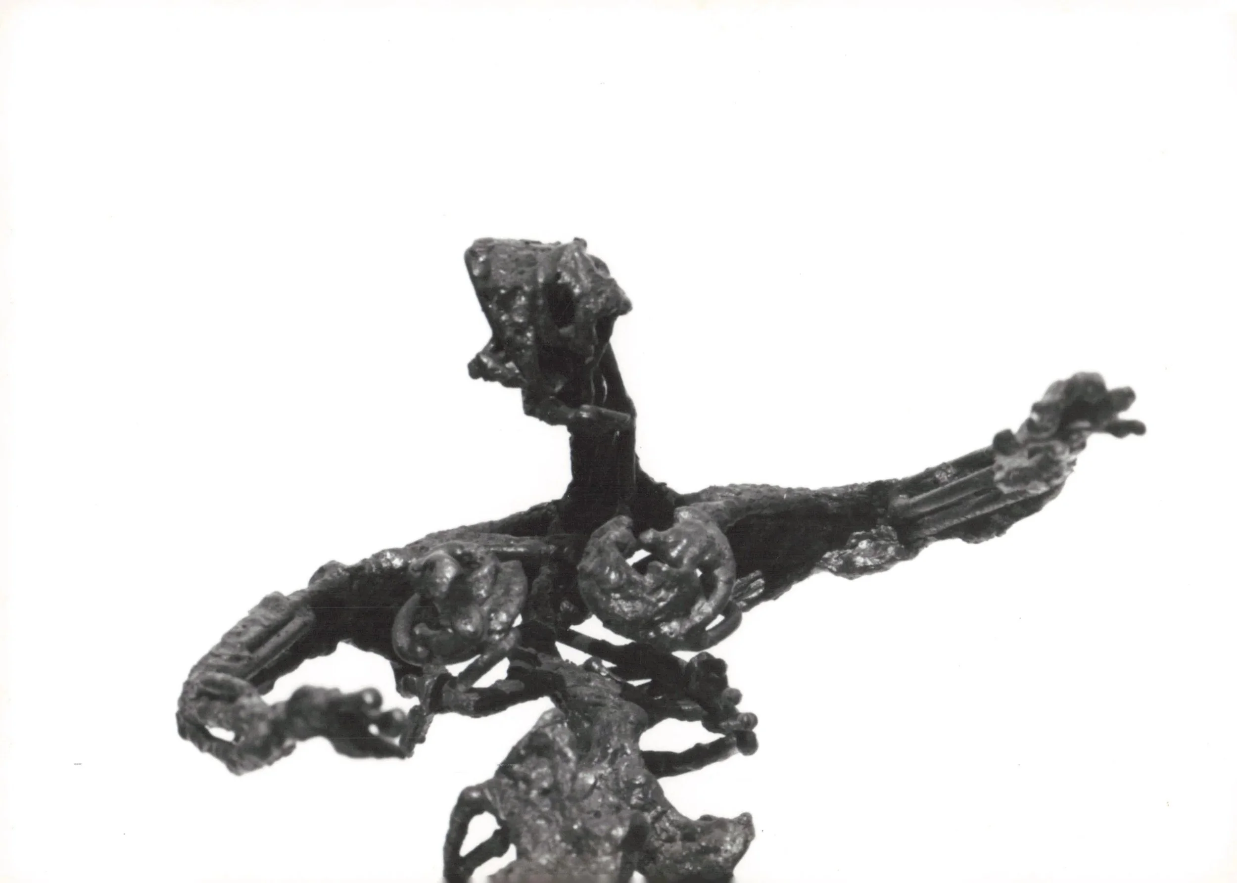 A small black metallic sculpture of a dog lying down, resting on a wrought iron fence with a white background.