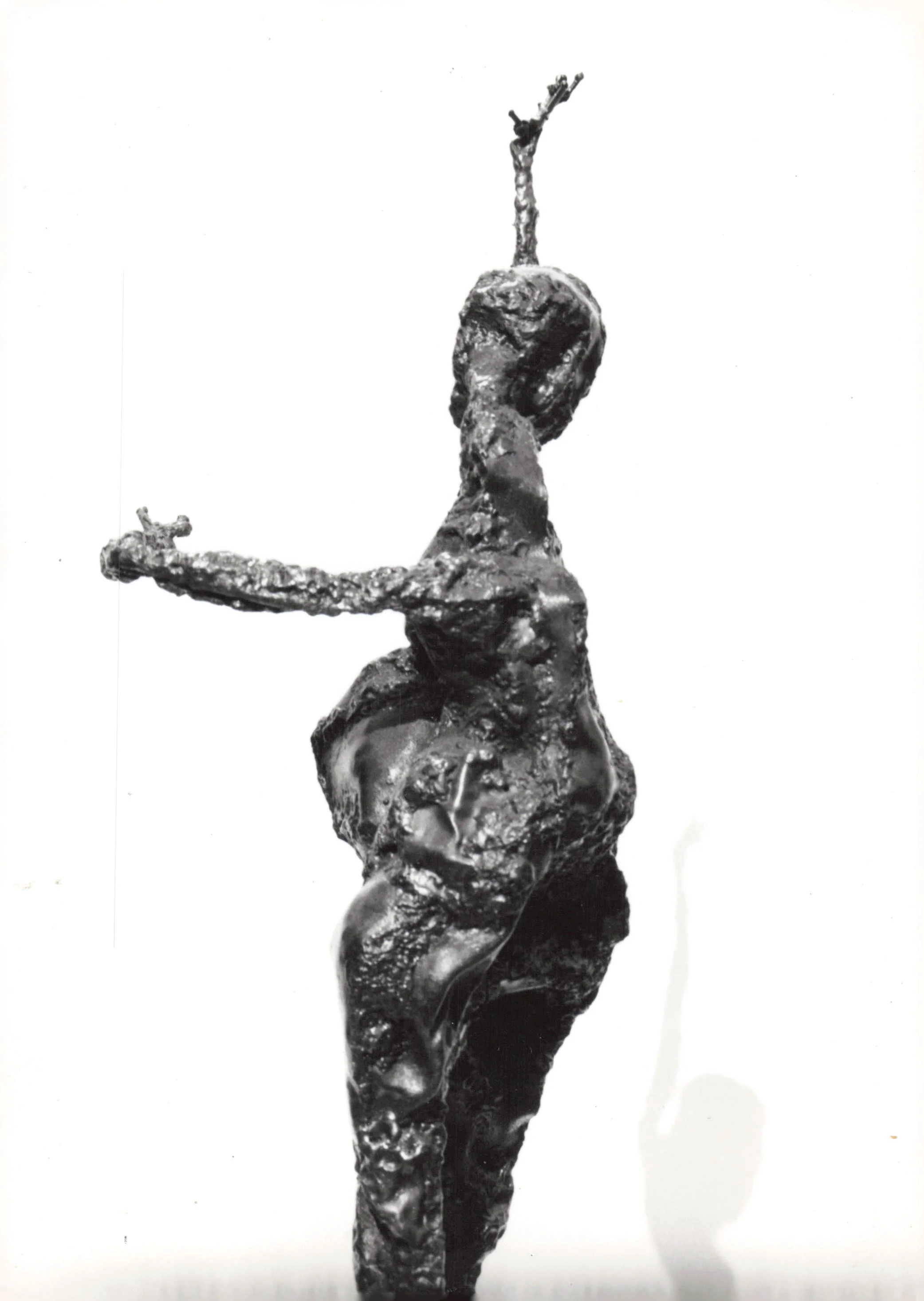 A metallic sculpture of a person with their arms extended, holding a cross in one hand and reaching upward with the other, captured in black and white.