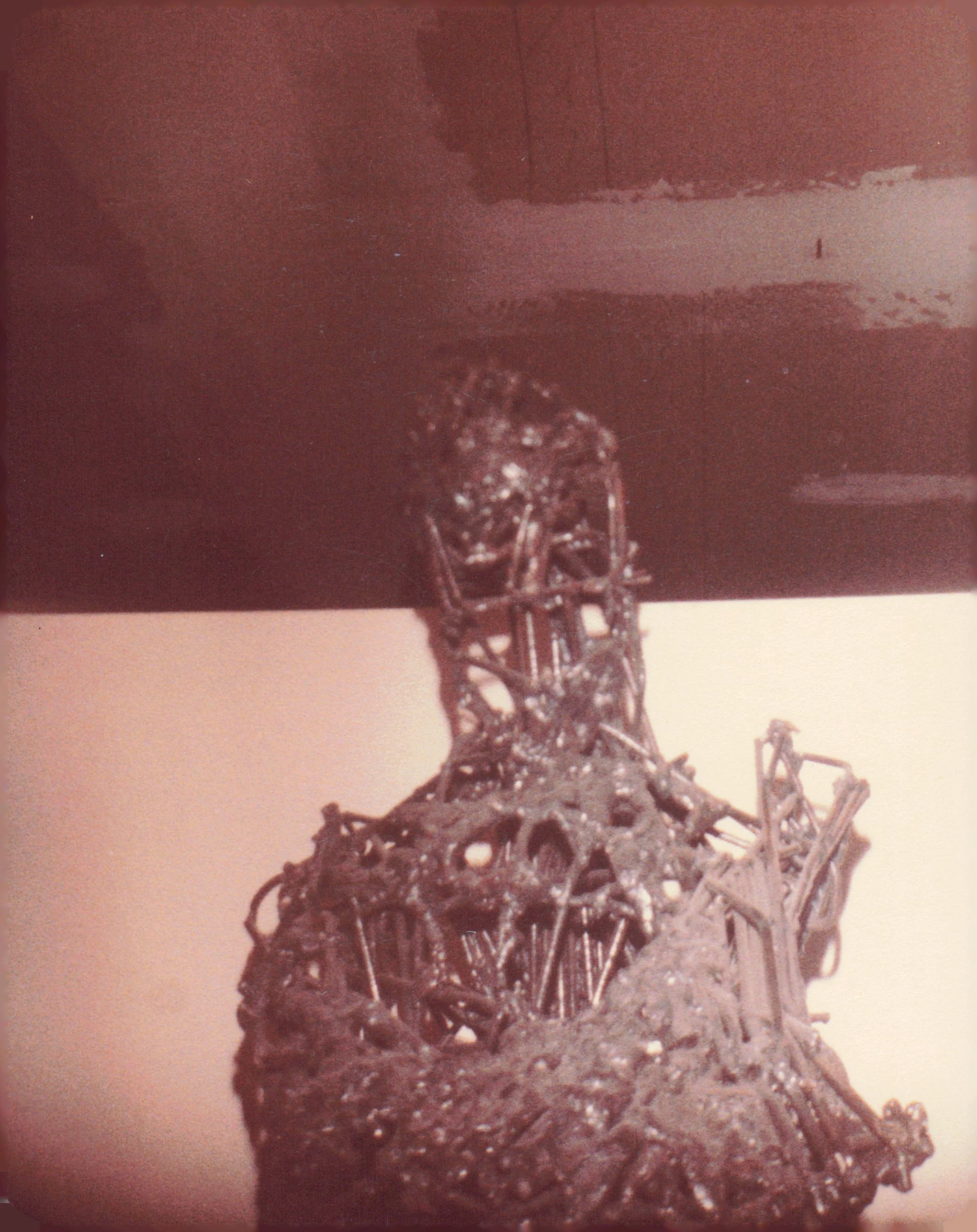 Close-up photo of a metallic sculpture resembling the Eiffel Tower, set against a plain background.