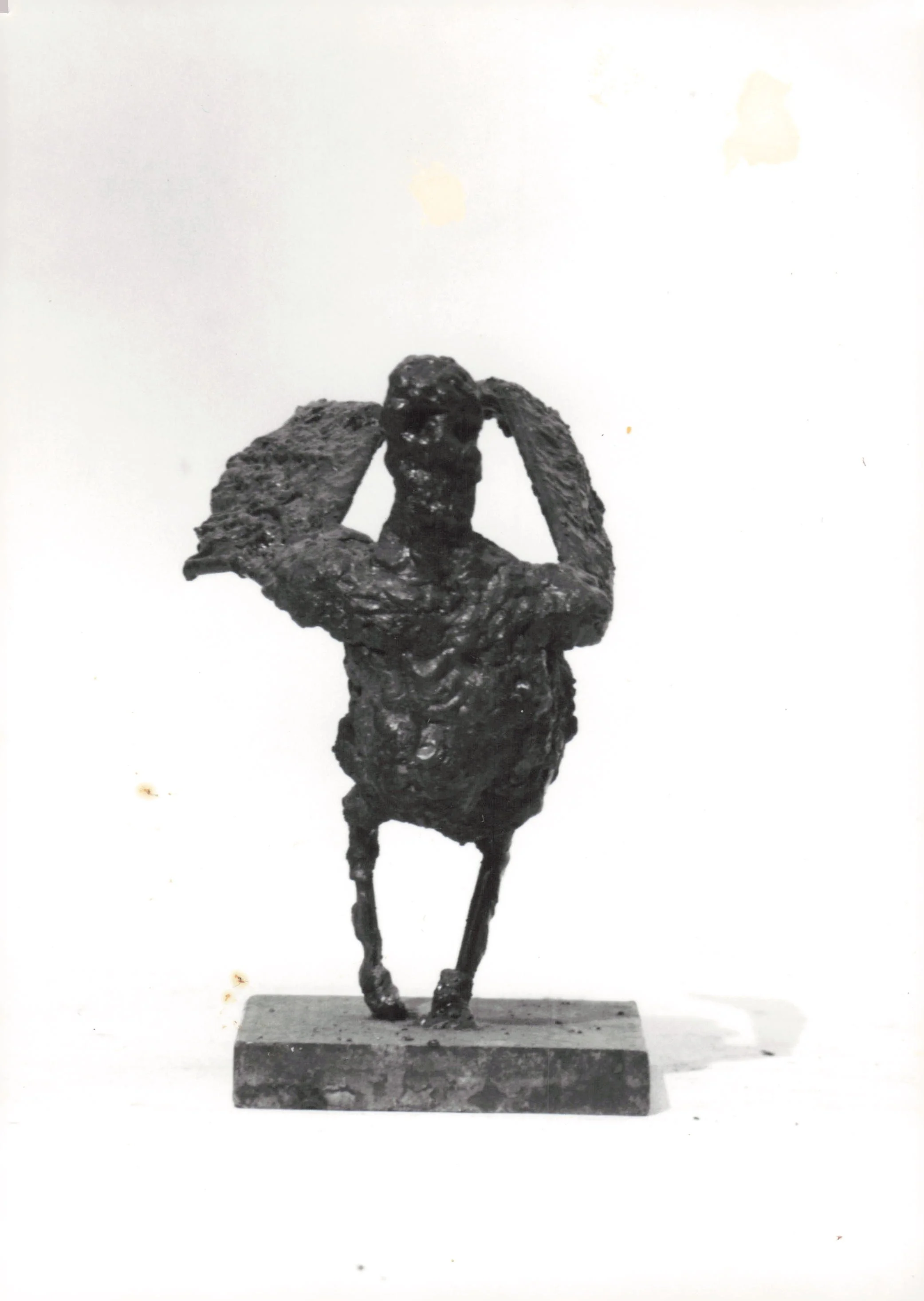 A bronze sculpture of a woman holding a large circular object above her head, standing on a rectangular base.