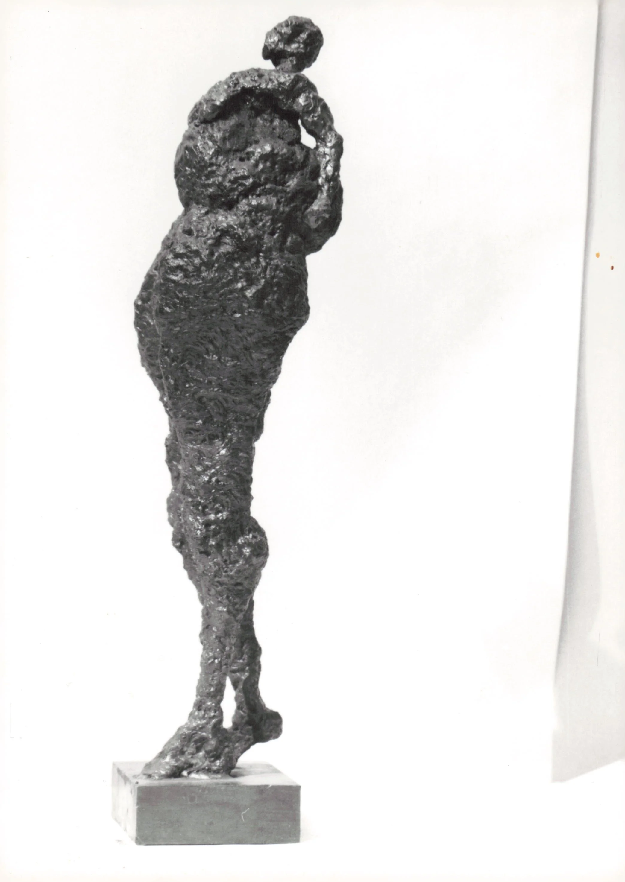 Black textured sculpture of a woman standing on a square base against a plain background.