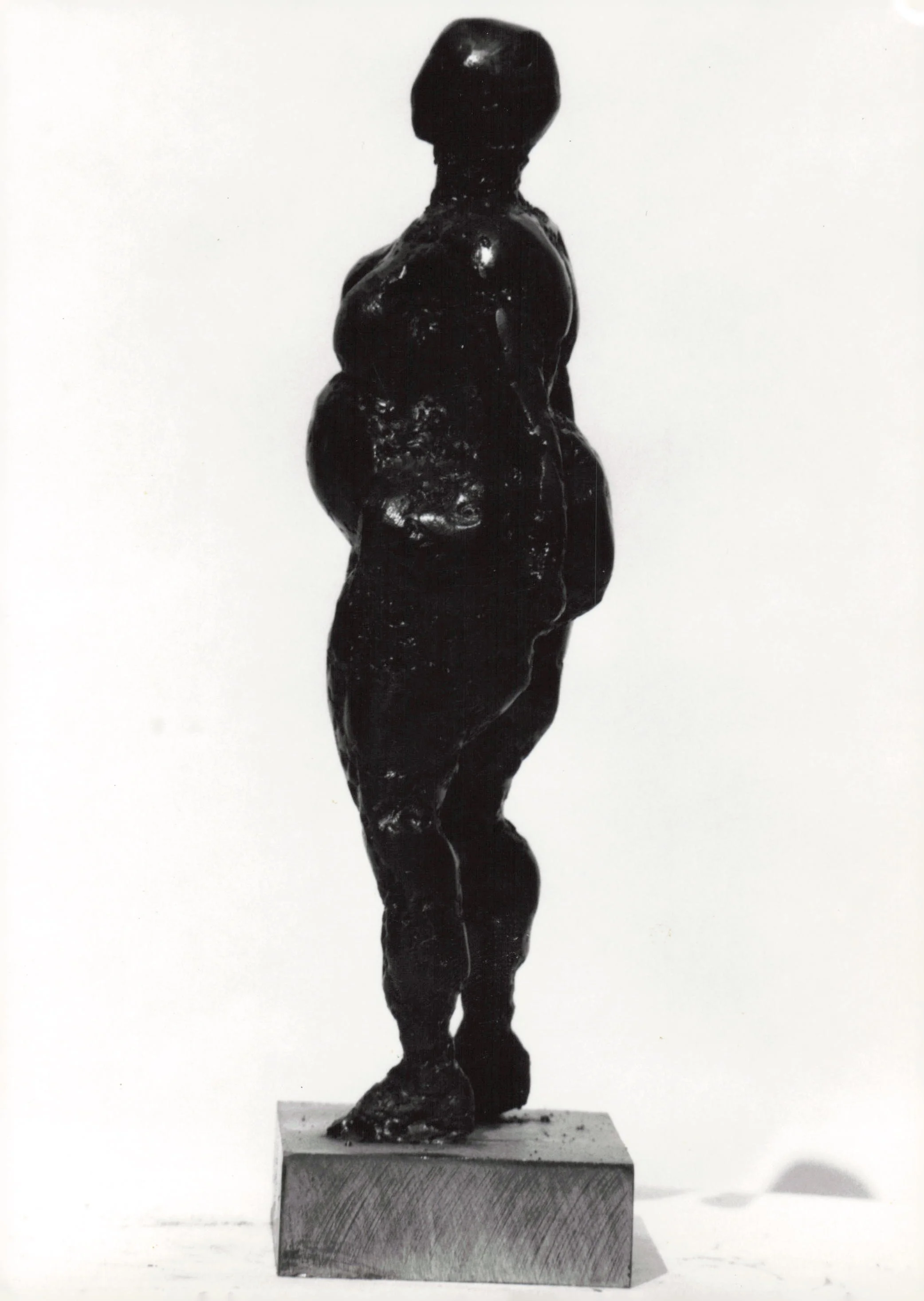 Black sculpture of a standing figure with arms crossed, mounted on a rectangular base.