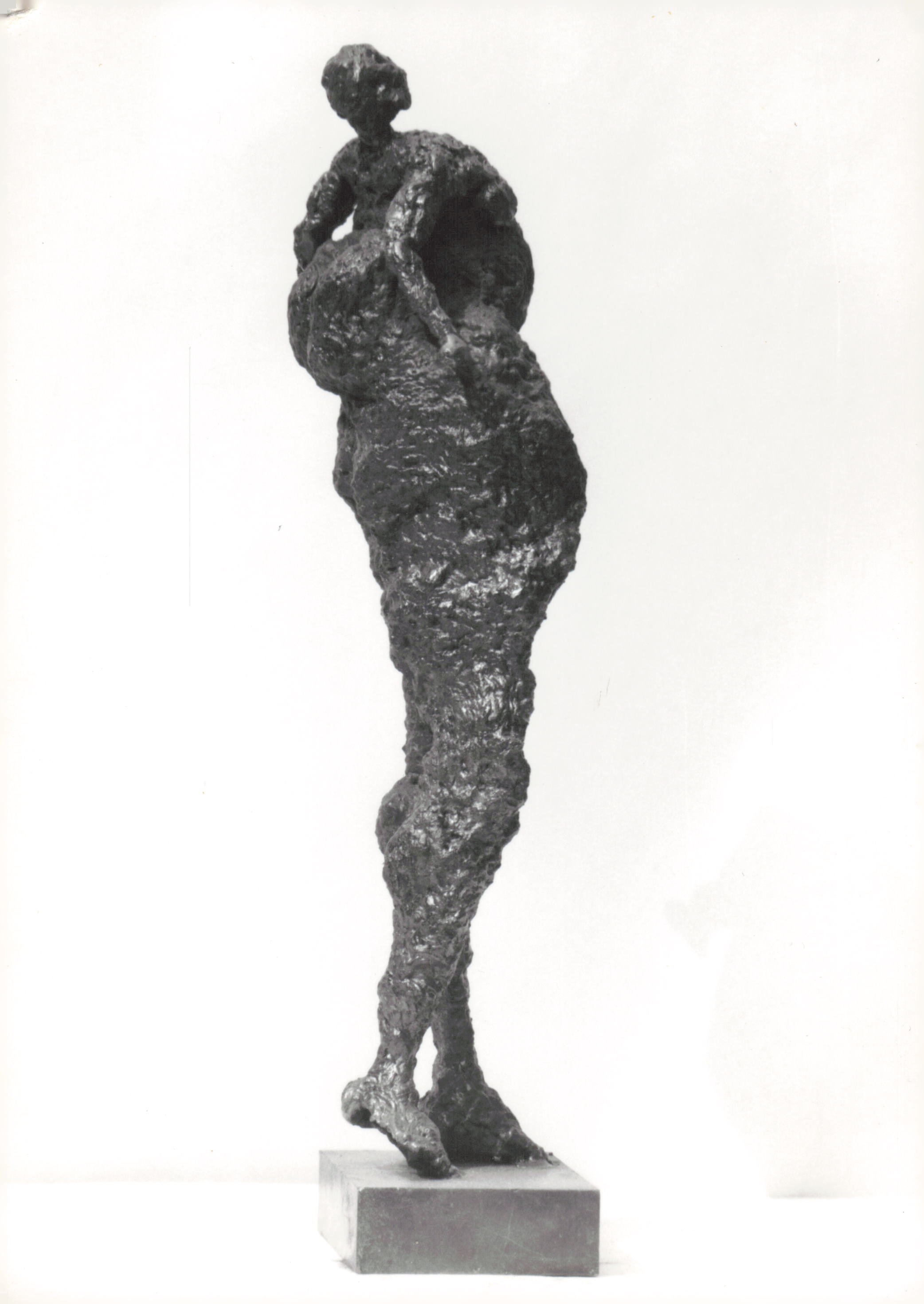 Black and white sculpture of a woman with a large vessel on her head, standing on a rectangular base.
