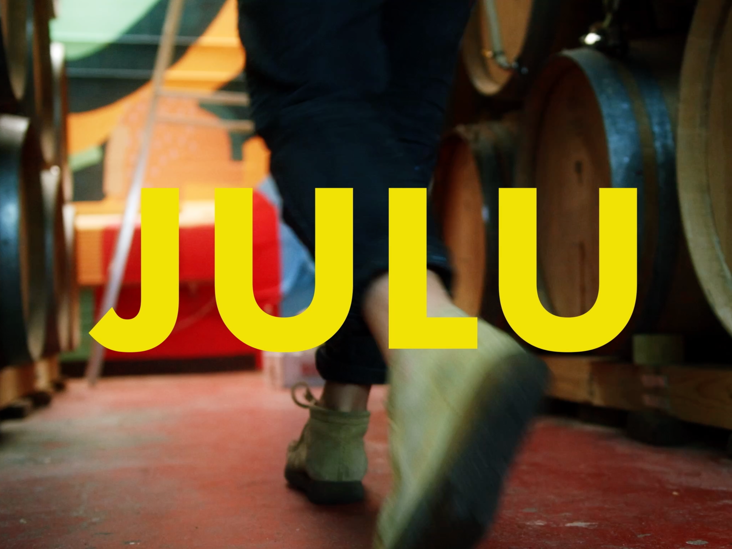 Beau Kester Cinematographer A person walking past wine barrels in a cellar with the date 'JULU' in large yellow letters overlaying the image.