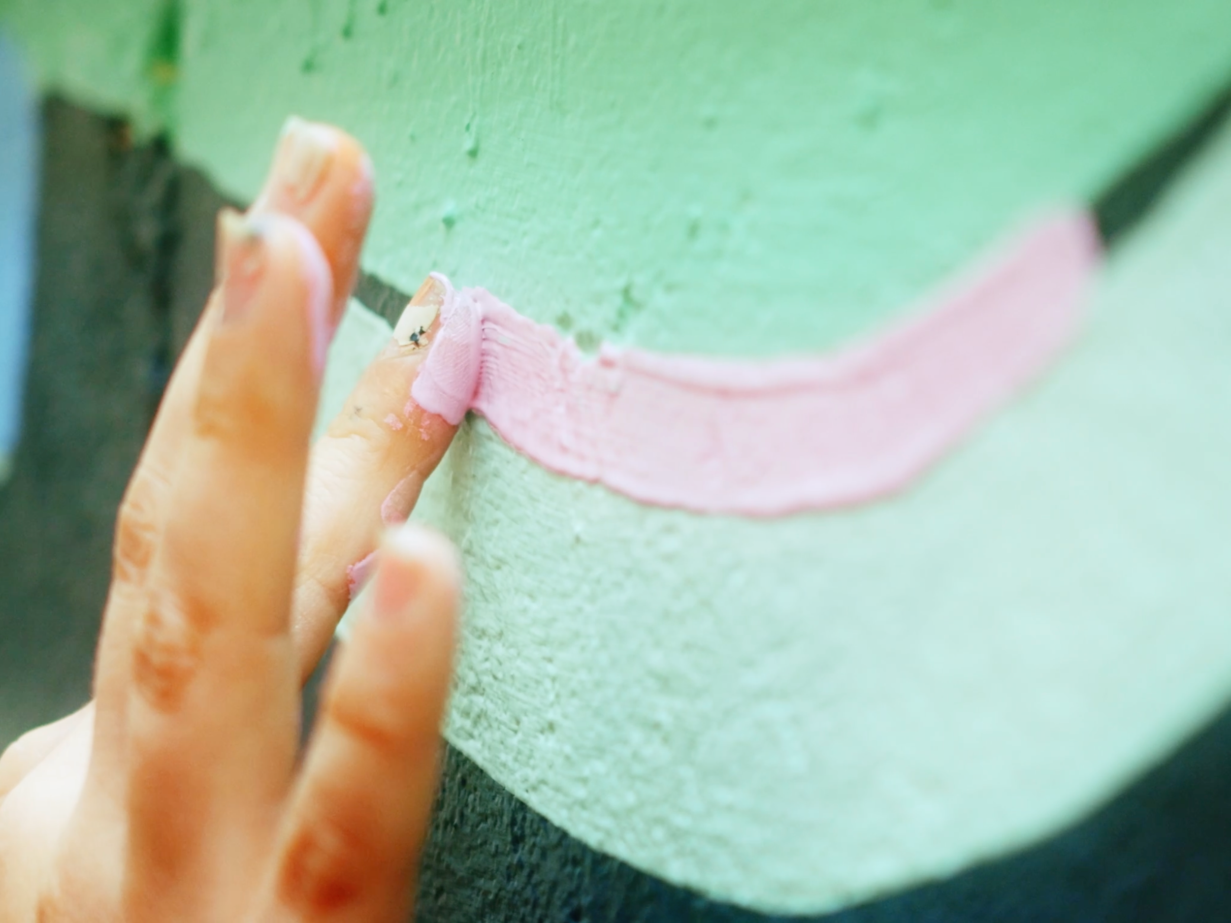 Beau Kester Cinematographer  A person with paint-stained fingers painting a smiley face on a wall, using pink paint for the mouth and green paint for the face.