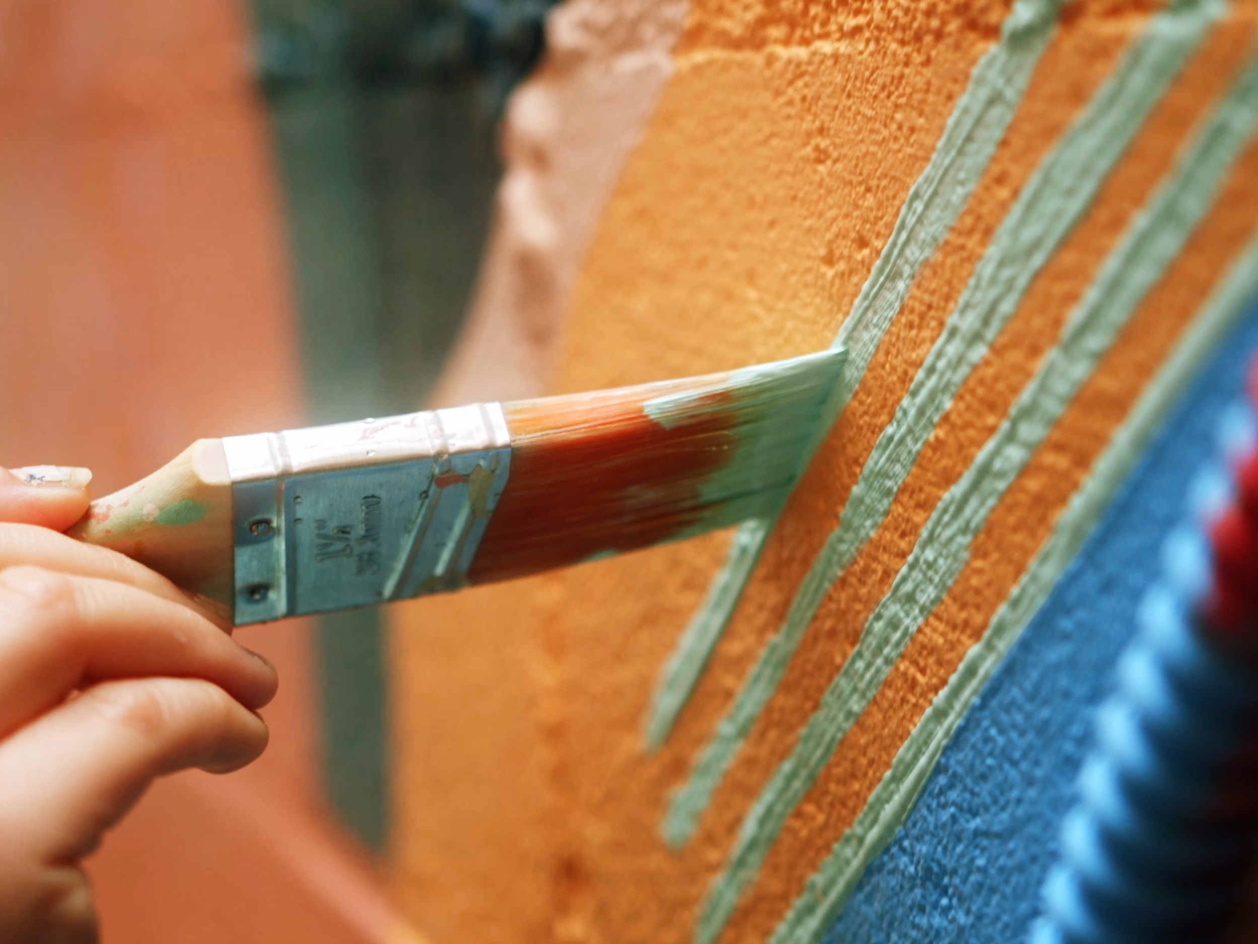 Beau Kester Cinematographer  Close-up of a hand painting a textured wall with orange and blue colors using a flat brush.