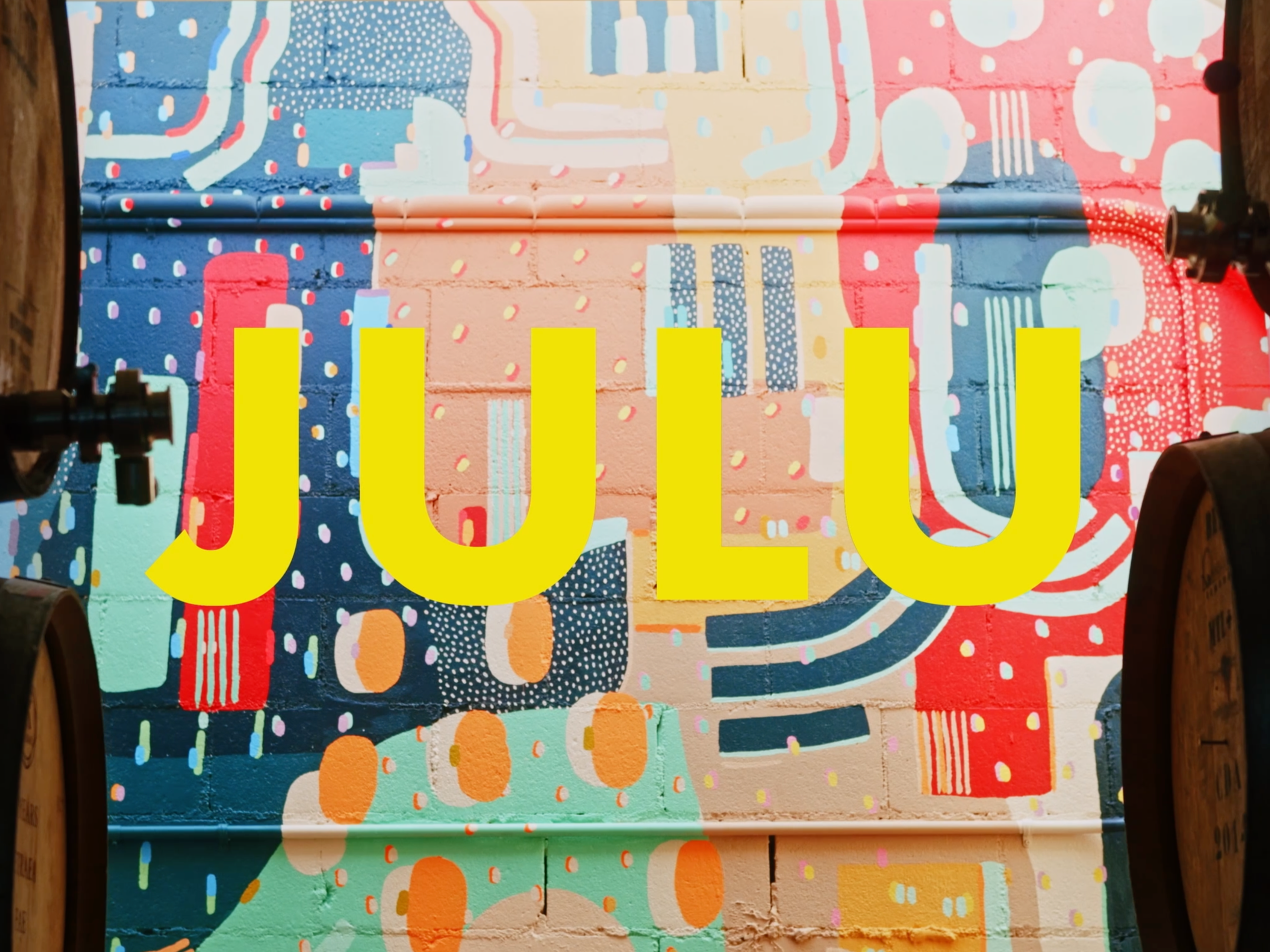 Colorful mural with pink, blue, green, red, and yellow abstract patterns. The word 'JULU' in large yellow letters is overlaid on the mural.