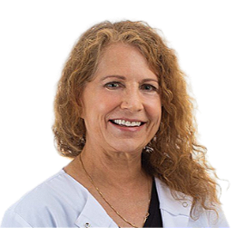 A woman with shoulder-length curly blonde hair, wearing a white medical coat and smiling.