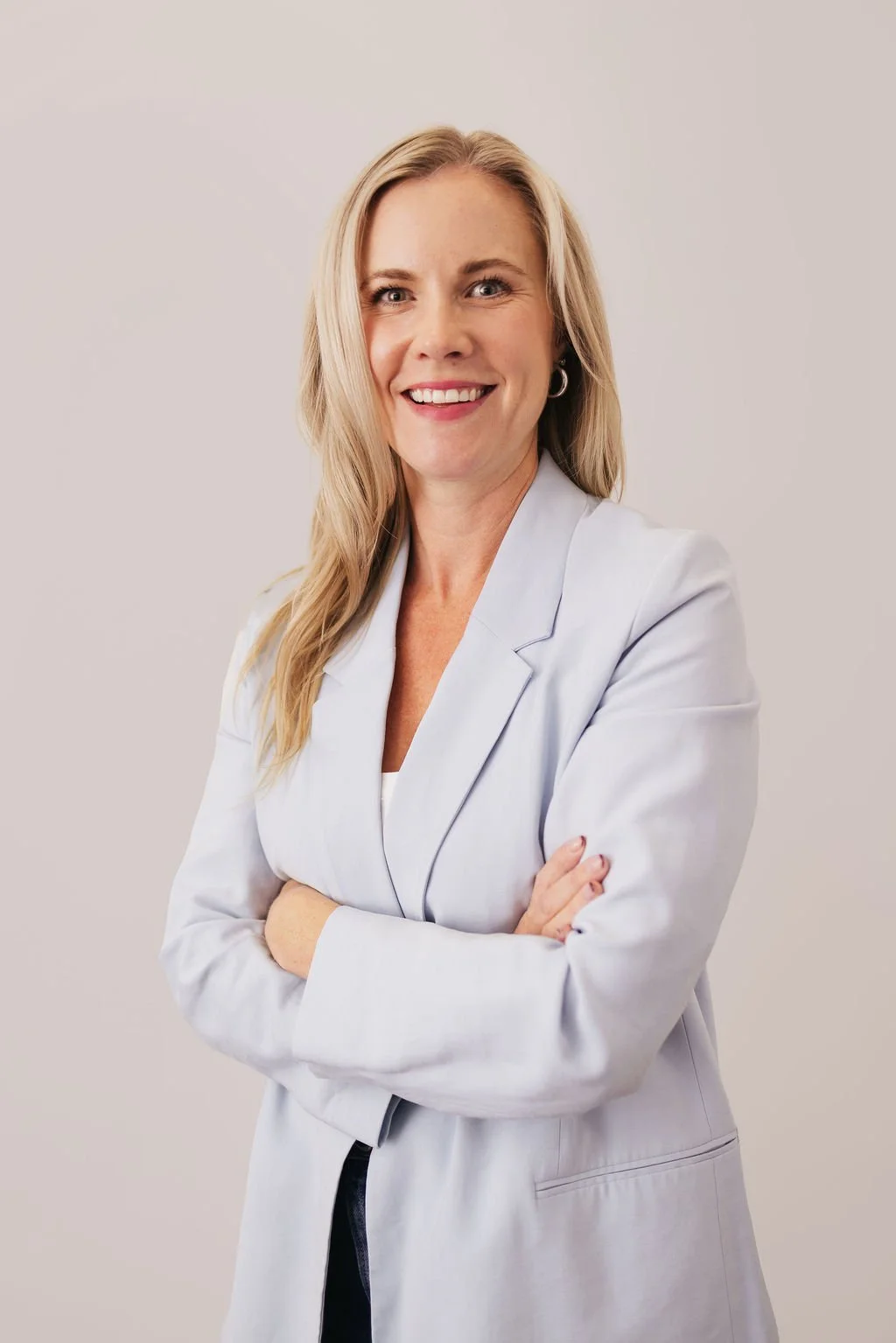 Smiling woman in a light blue blazer with arms crossed.