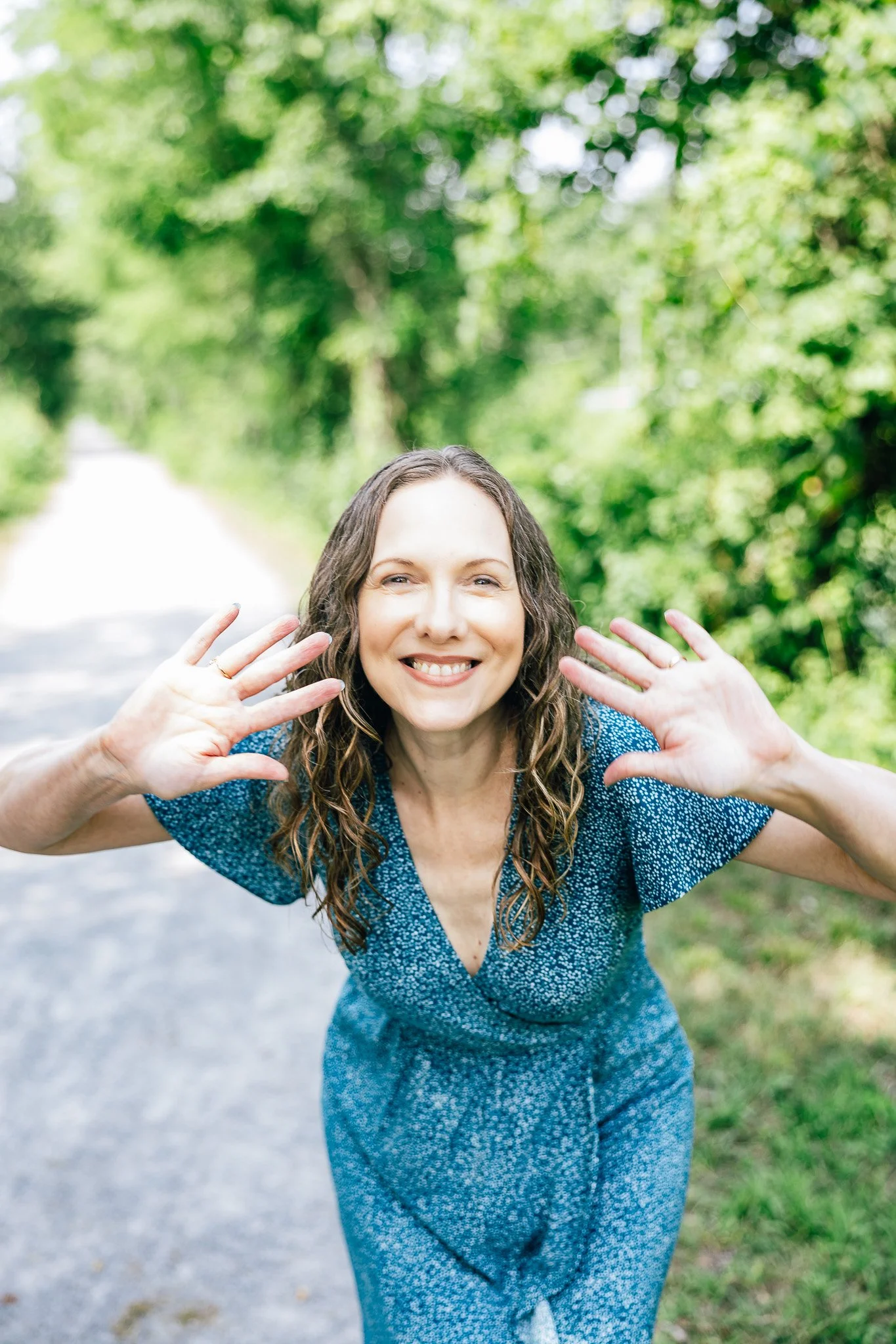 Jen leaning forward. holding hands by face, smiling and waving hi