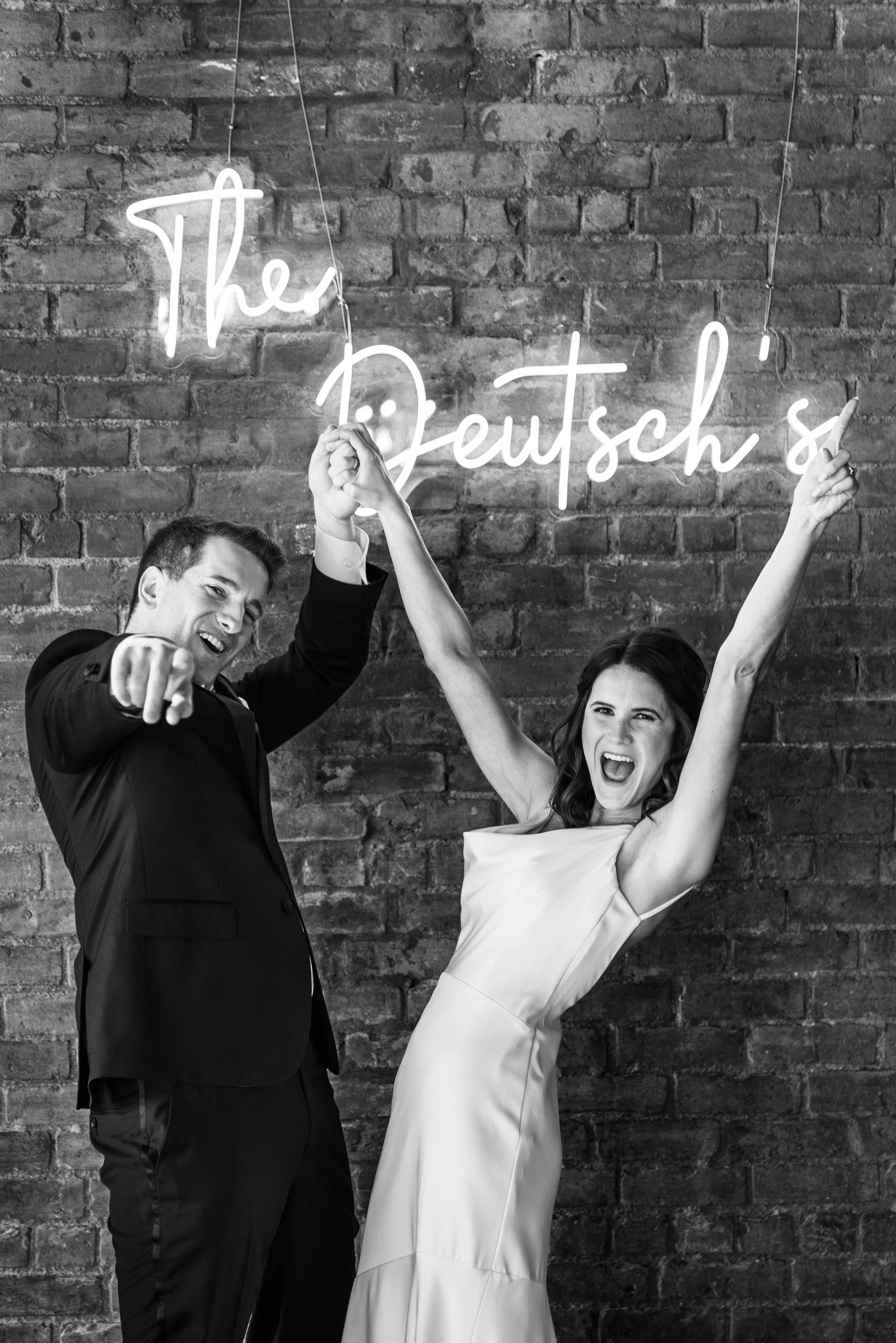 Black and white image of married couple celebrating in front of neon sign with their name at their reception