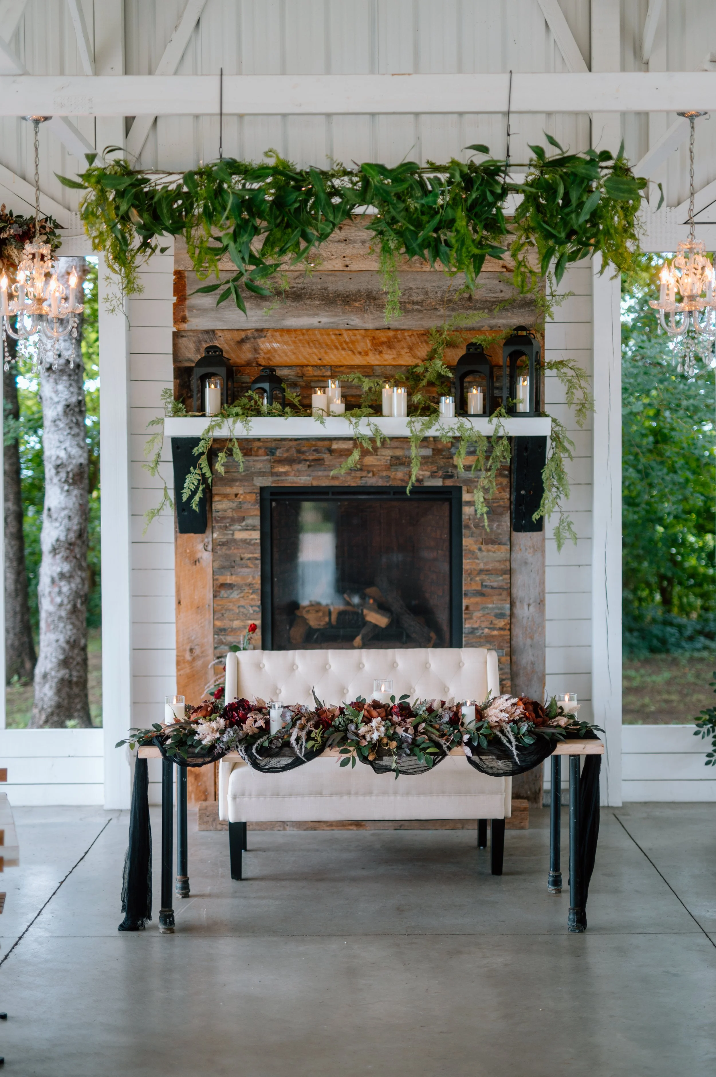 Sweetheart table with black draping, burgundy and pink florals, a cream loveseat, and ivory candles