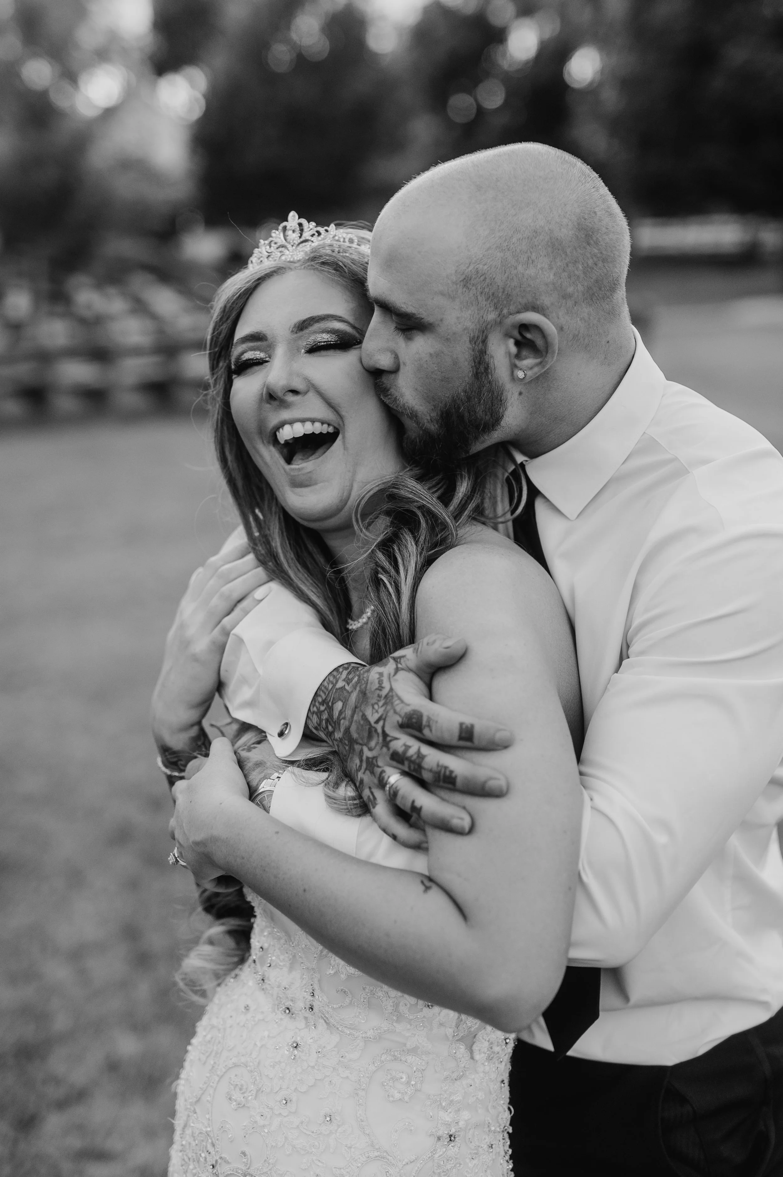 Black and white image of bride laughing after the groom sneaks up behind her and gives her a hug