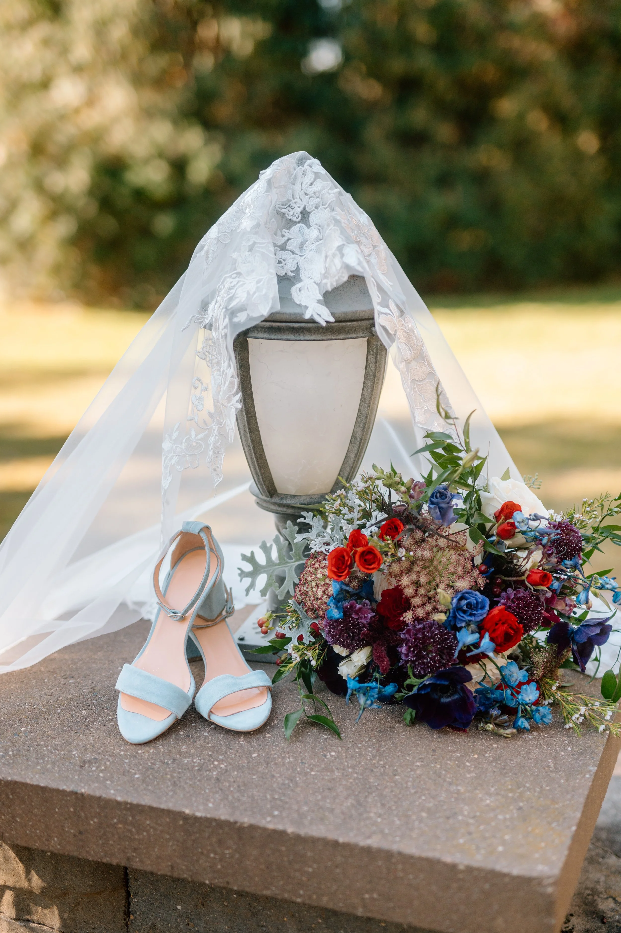Stone Lion Winery wedding day detail photo of lace-trimmed veil draped on lantern behind light blue suede heels and colorful fall bouquet of flowers