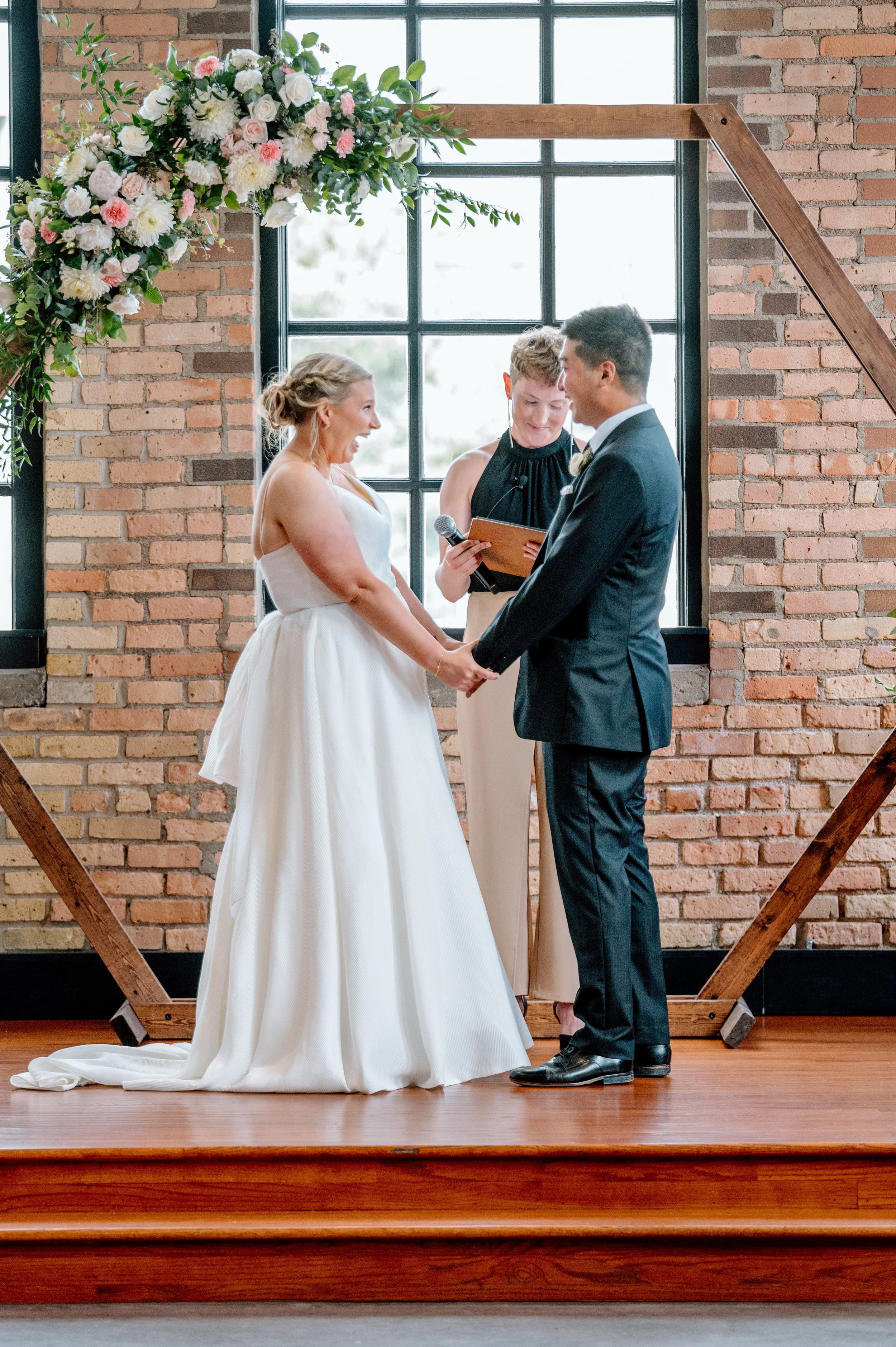 Bride and groom hold hands and laugh together during their Essence Event Center wedding ceremomy