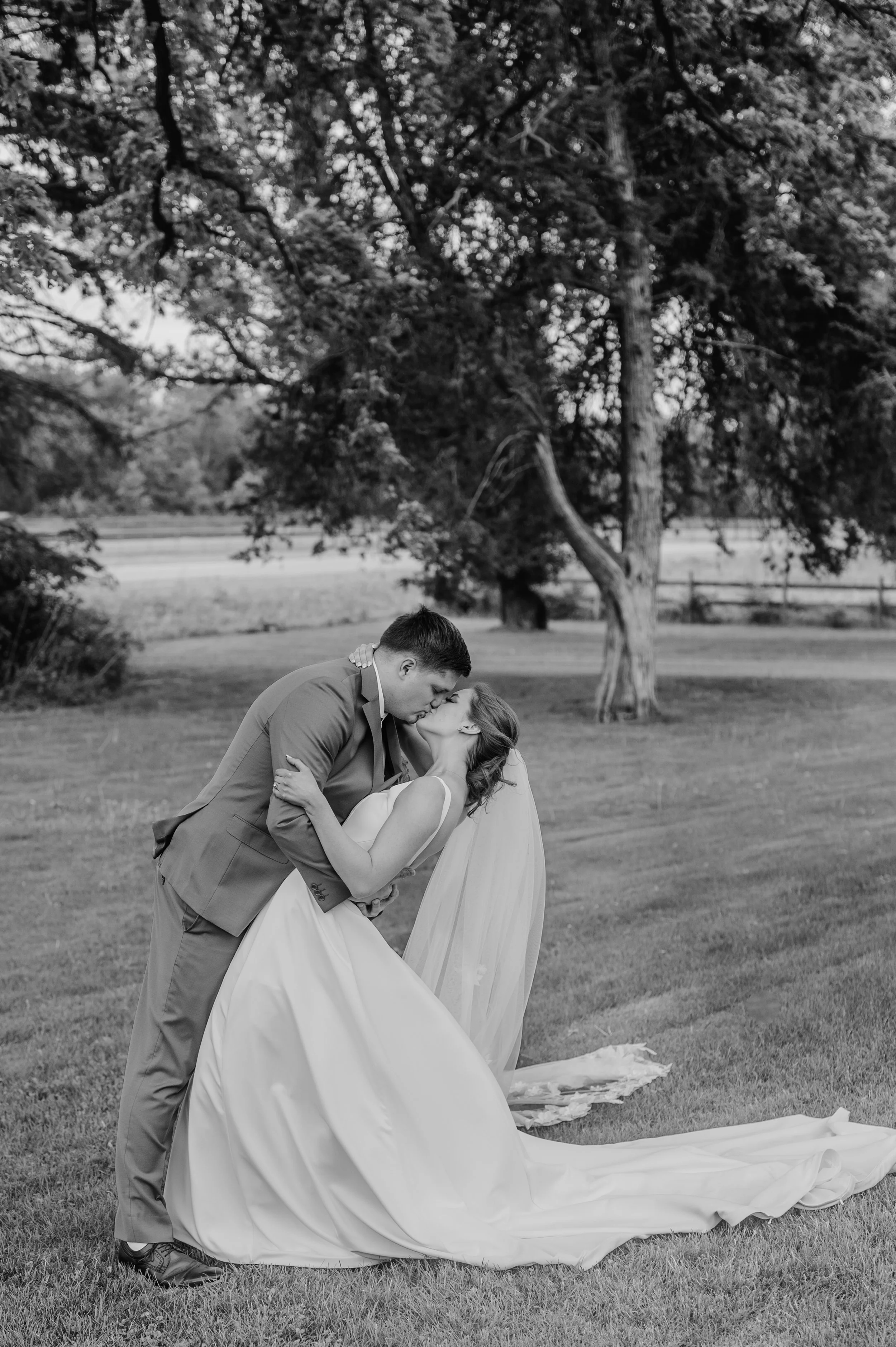 Black and white image of the groom dipping the bride for a kiss on the lawn out in front of the main house at Genesis Ranch in Minnesota