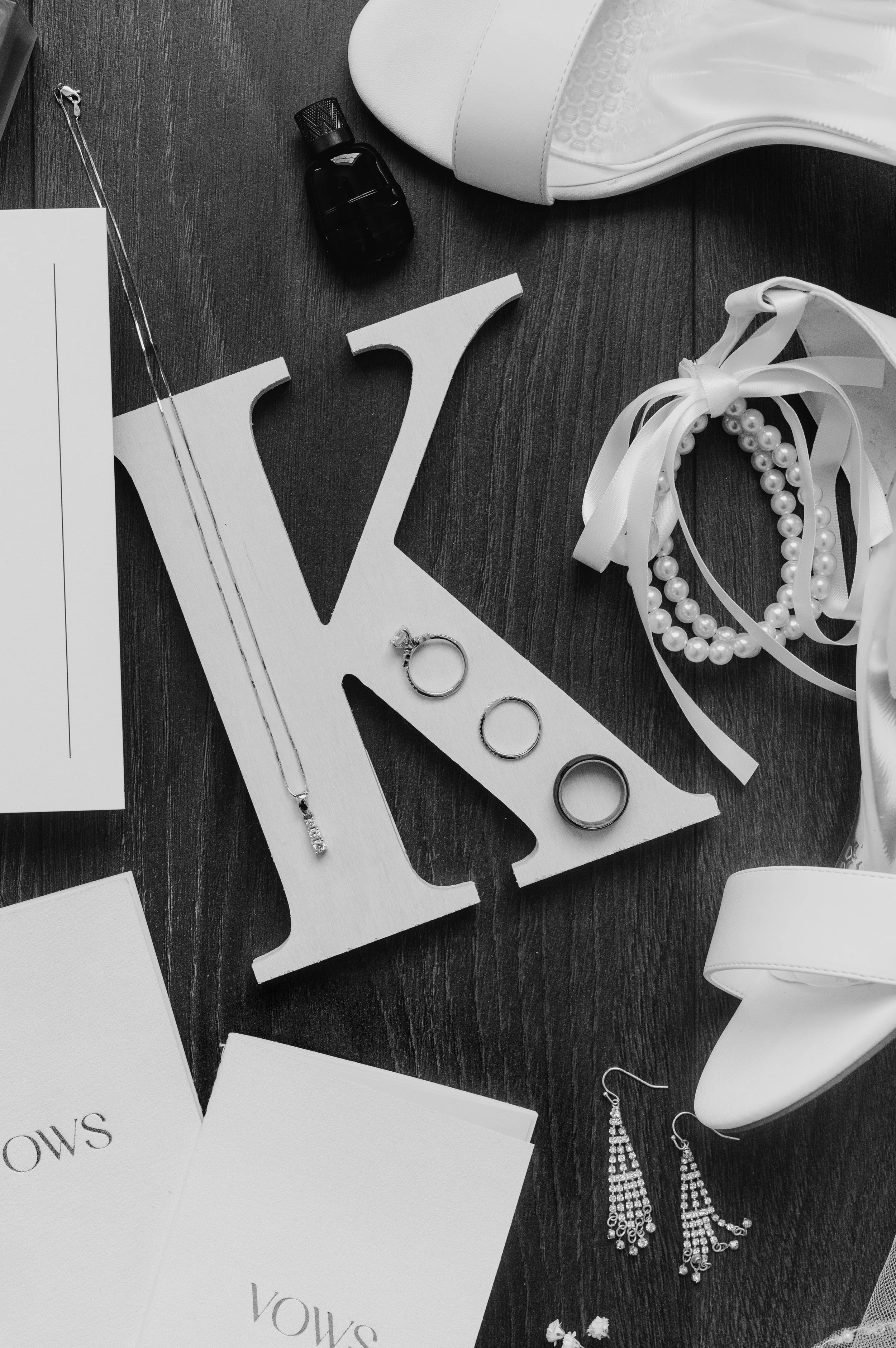 Black and white wedding day details flatlay photo of jewelry, bride's shoes, and vow books