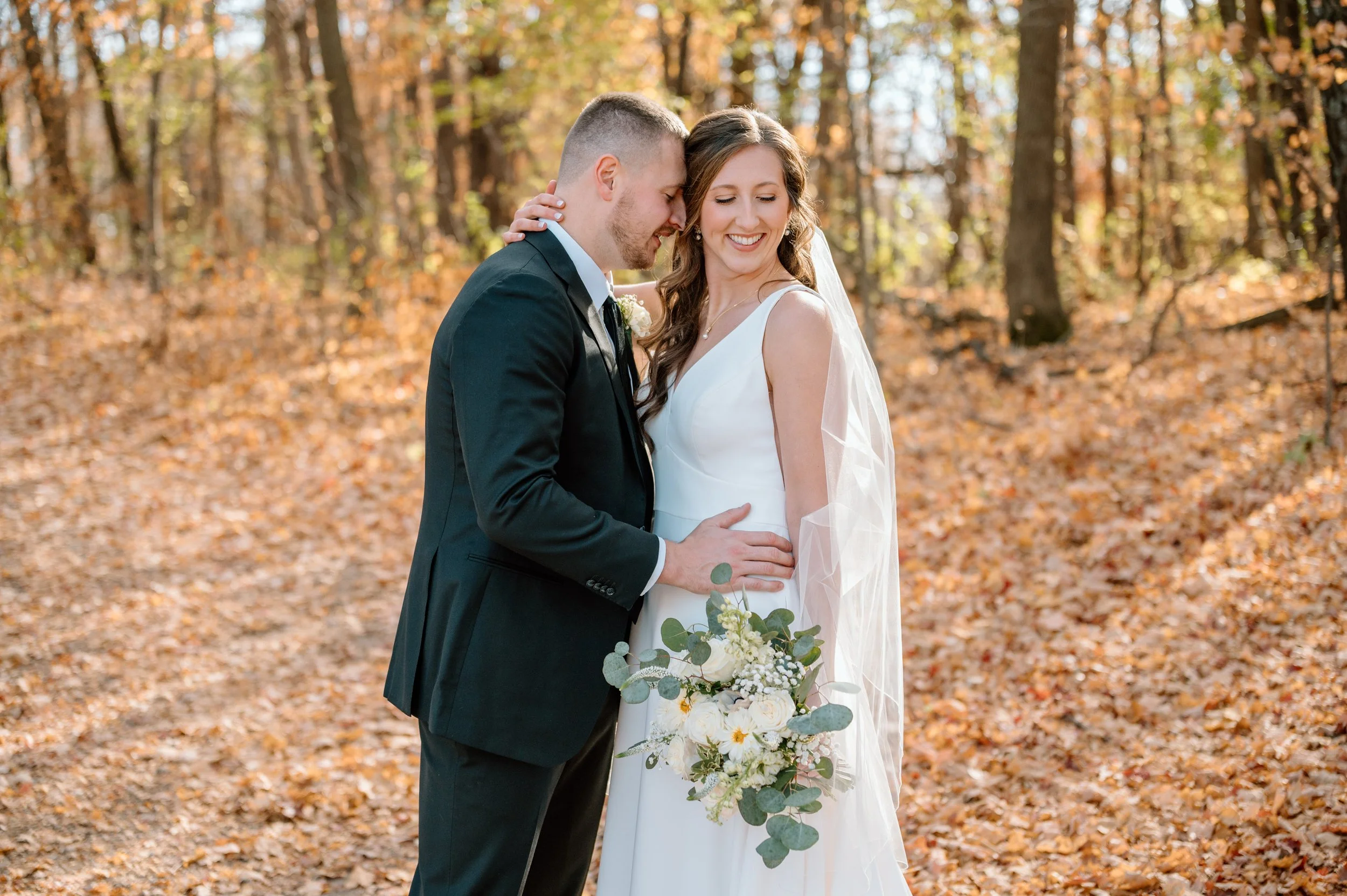 Bride and groom snuggle together among the golden and yellow fall leaves of a Minnesota fall at the Horse and Hunt Club in Prior Lake, MN
