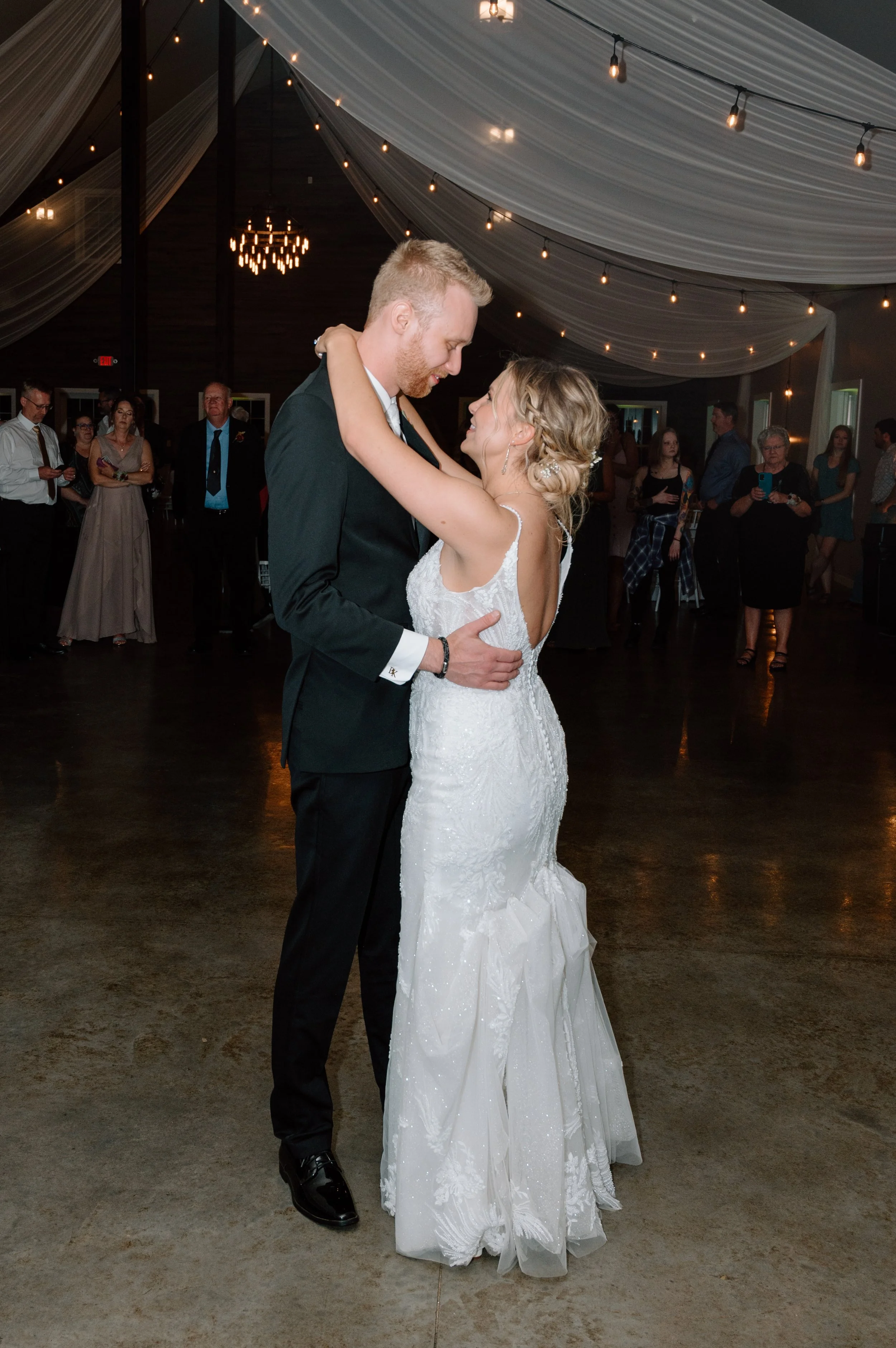 Bride and groom share their first dance under white draping and string lights at the Falls wedding venue
