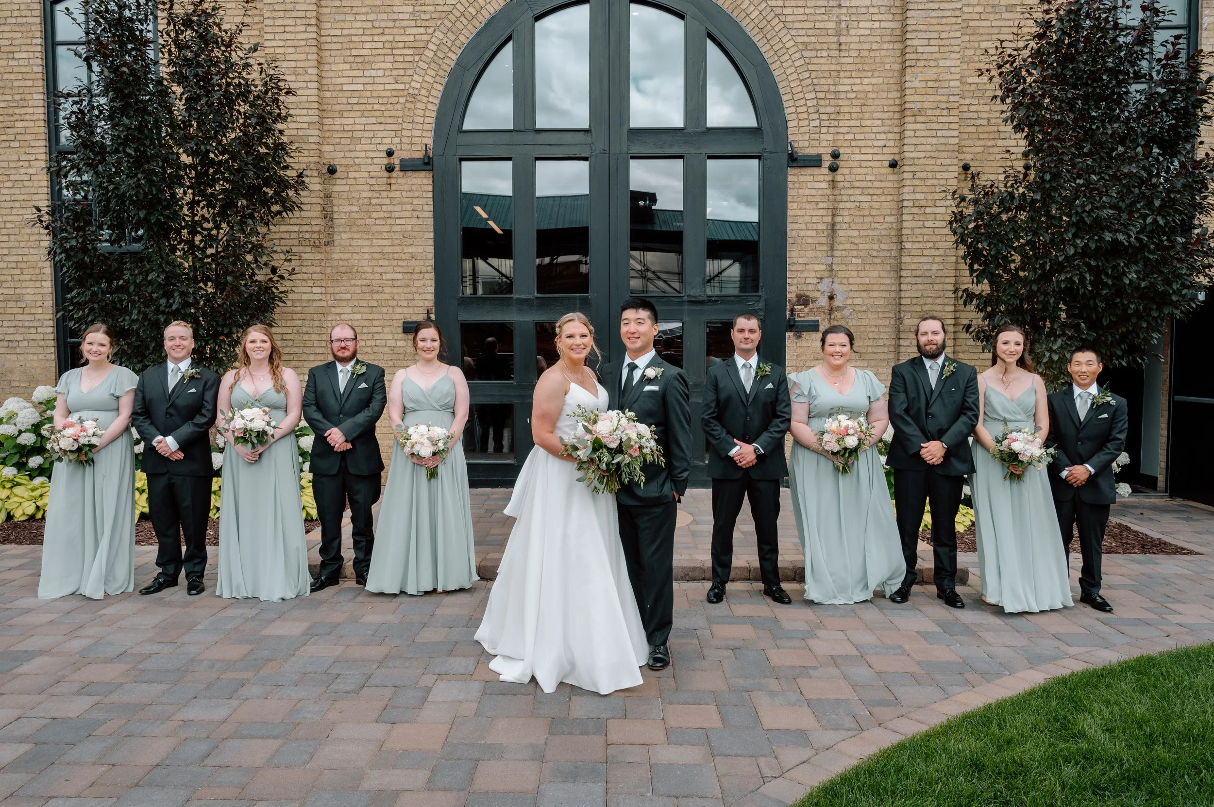 Sage green wedding party in the brick courtyard outside the Essence Event Center in St. Paul, MN