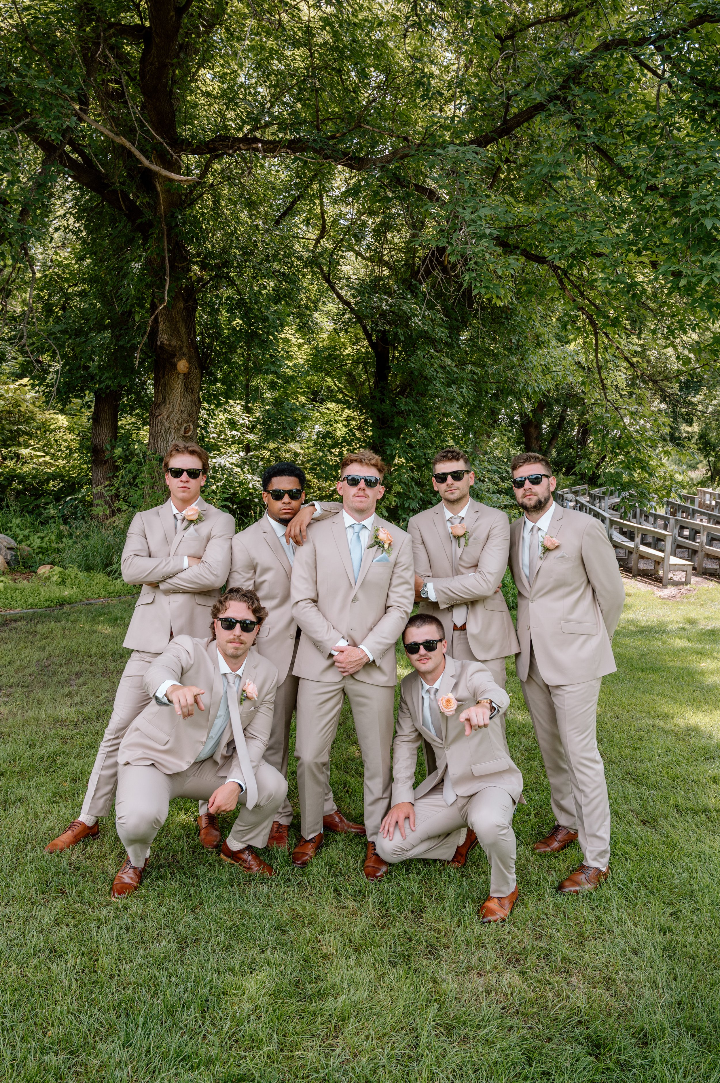Groomsmen in tan tuxes with champagne ties, pink boutonnieres, and sunglasses at Gathered Oaks in Alexandria, MN during a summer wedding