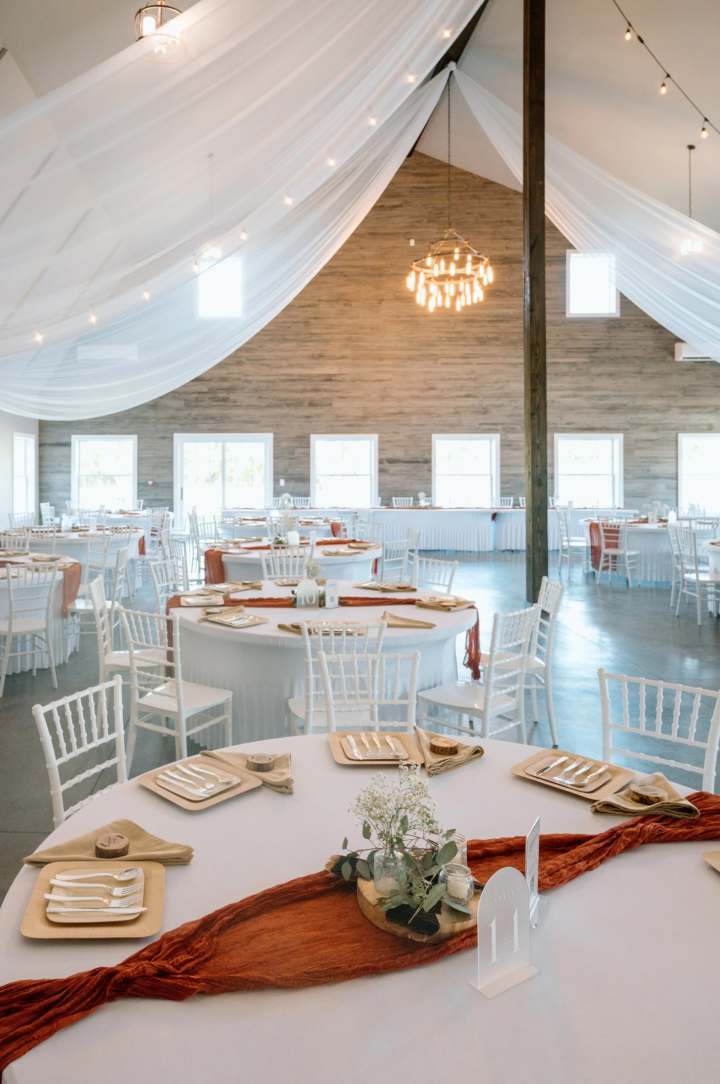 Brightly light reception space with white ceiling draping, round tables with white chairs at Twin Cities area wedding venue