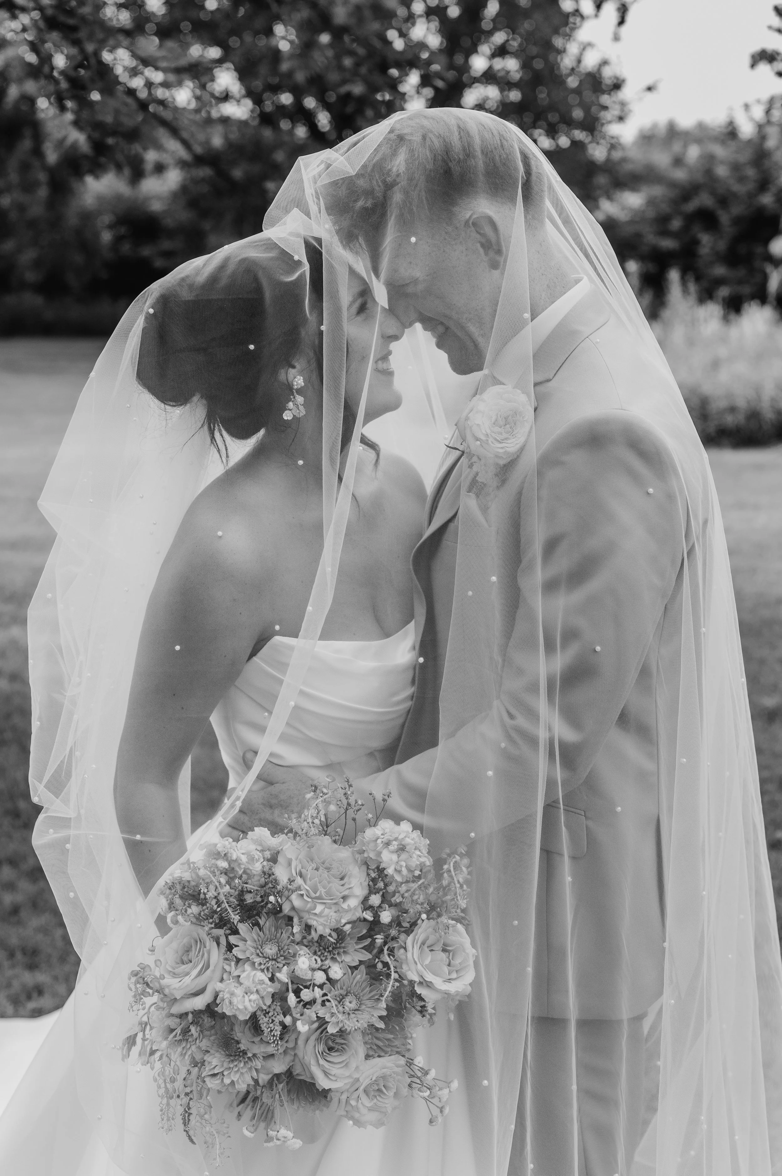 Black and white image of bride and groom smiling at each other underneath pearl-encrusted cathedral-lengthveil