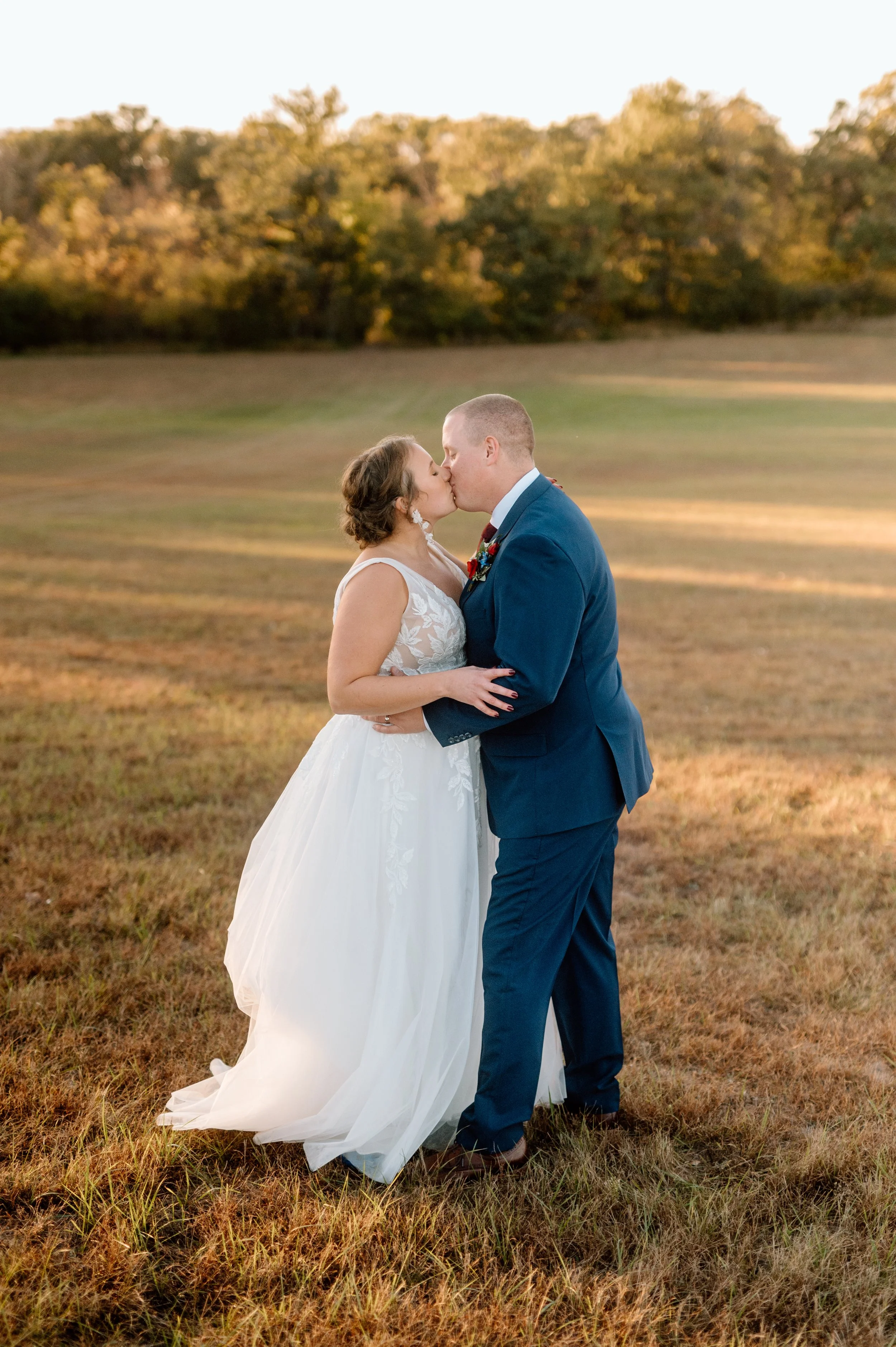Bride and groom frolic in a field and share a kiss at sunset on their October wedding day in Minneapolis, Minnesota