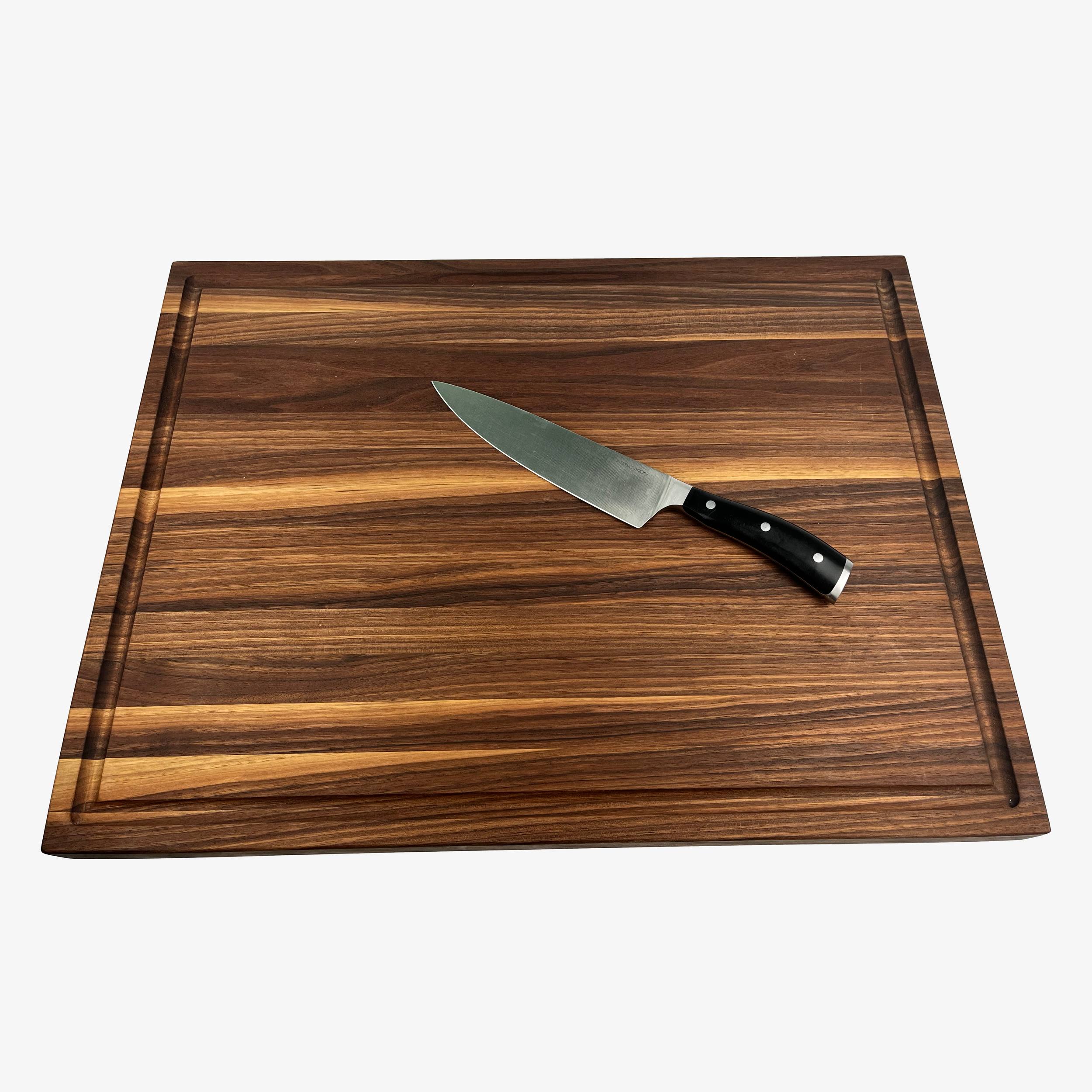 Large walnut board with juice groove shown with a chef's knife.