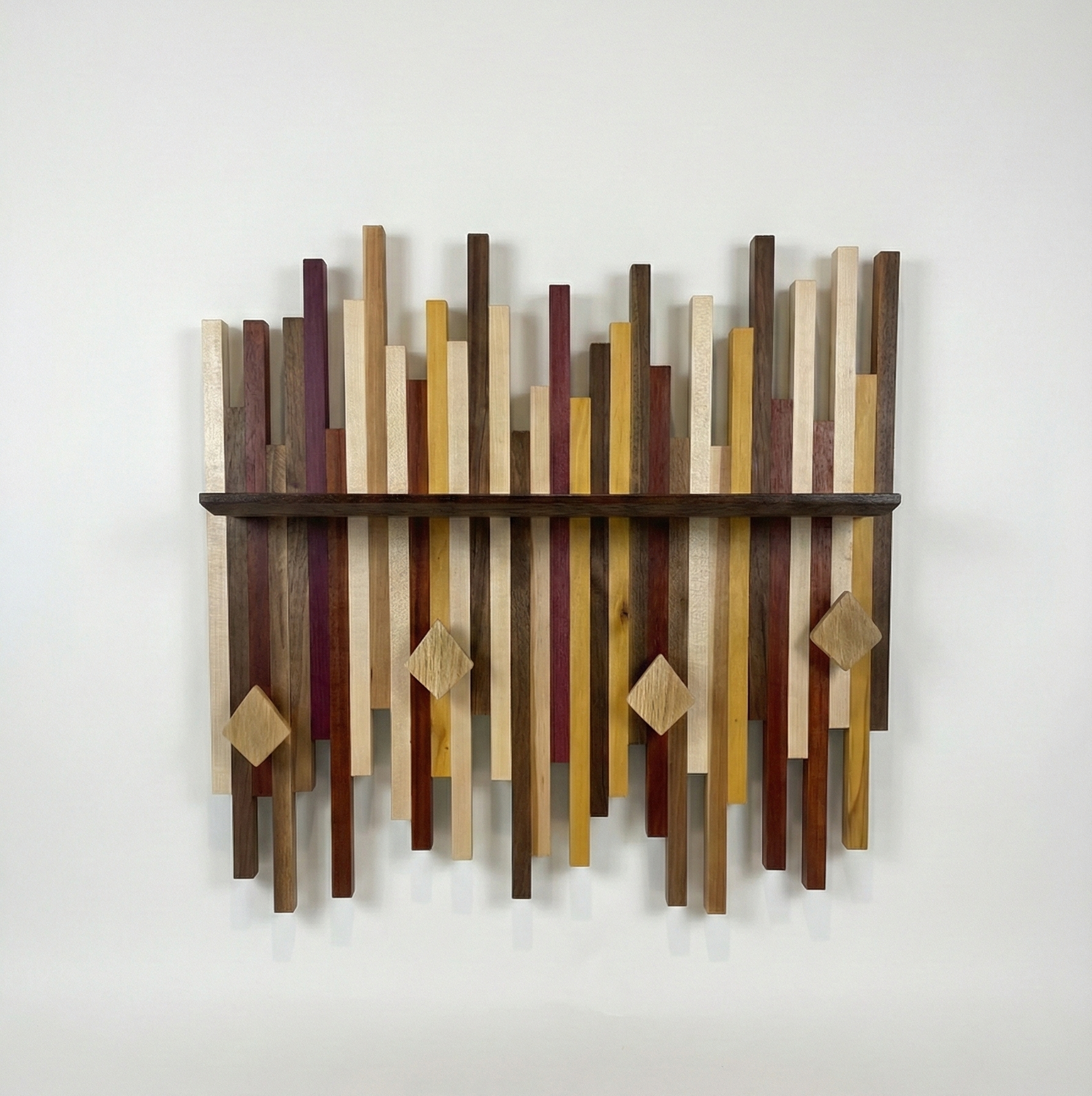 Wall shelf made of various colorful species of wood with a black shelf and white oak diamond-shaped hooks