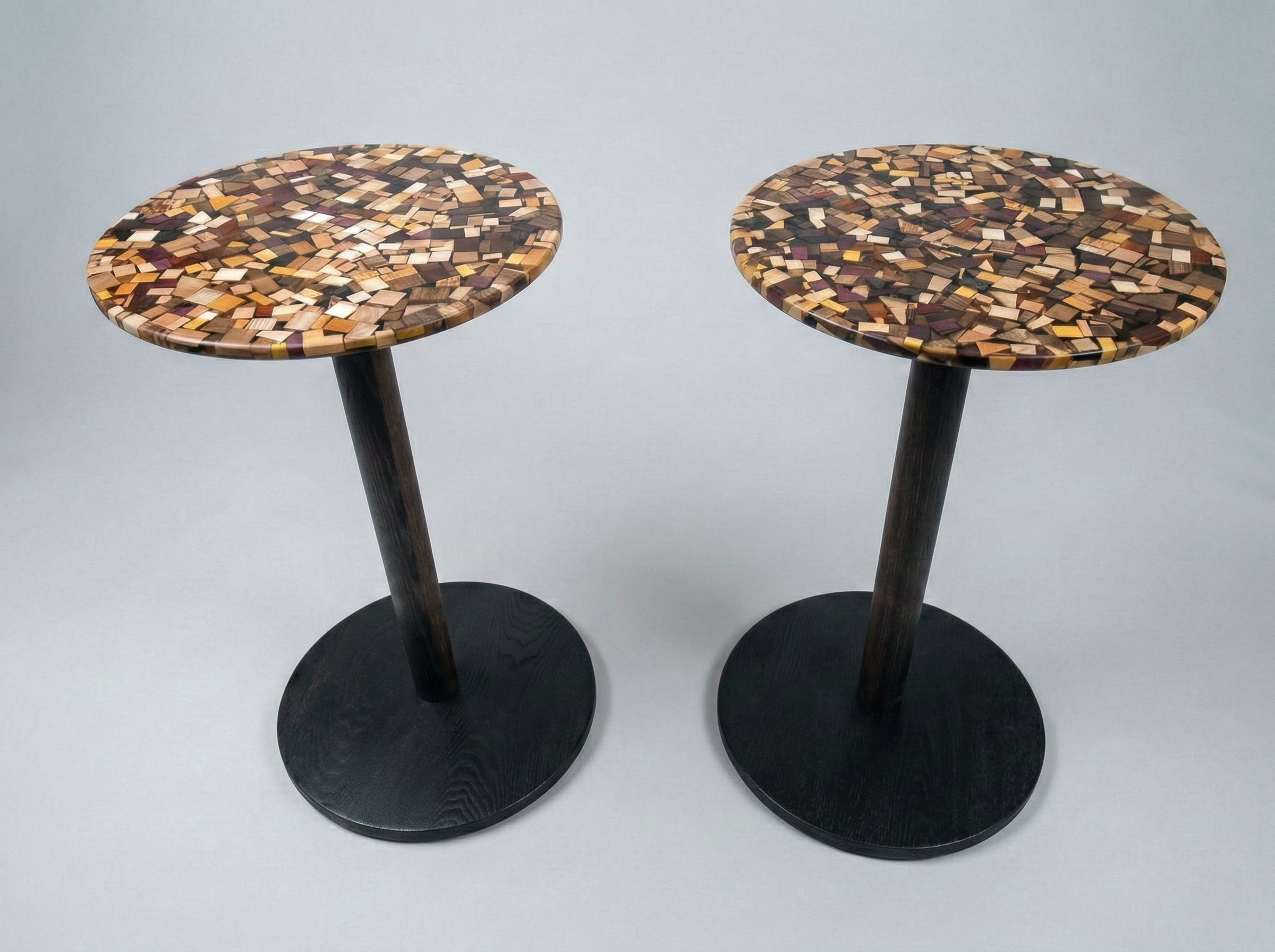 Round wooden end tables with black bottoms and posts and tops made of pieces of different species of wood encased in epoxy