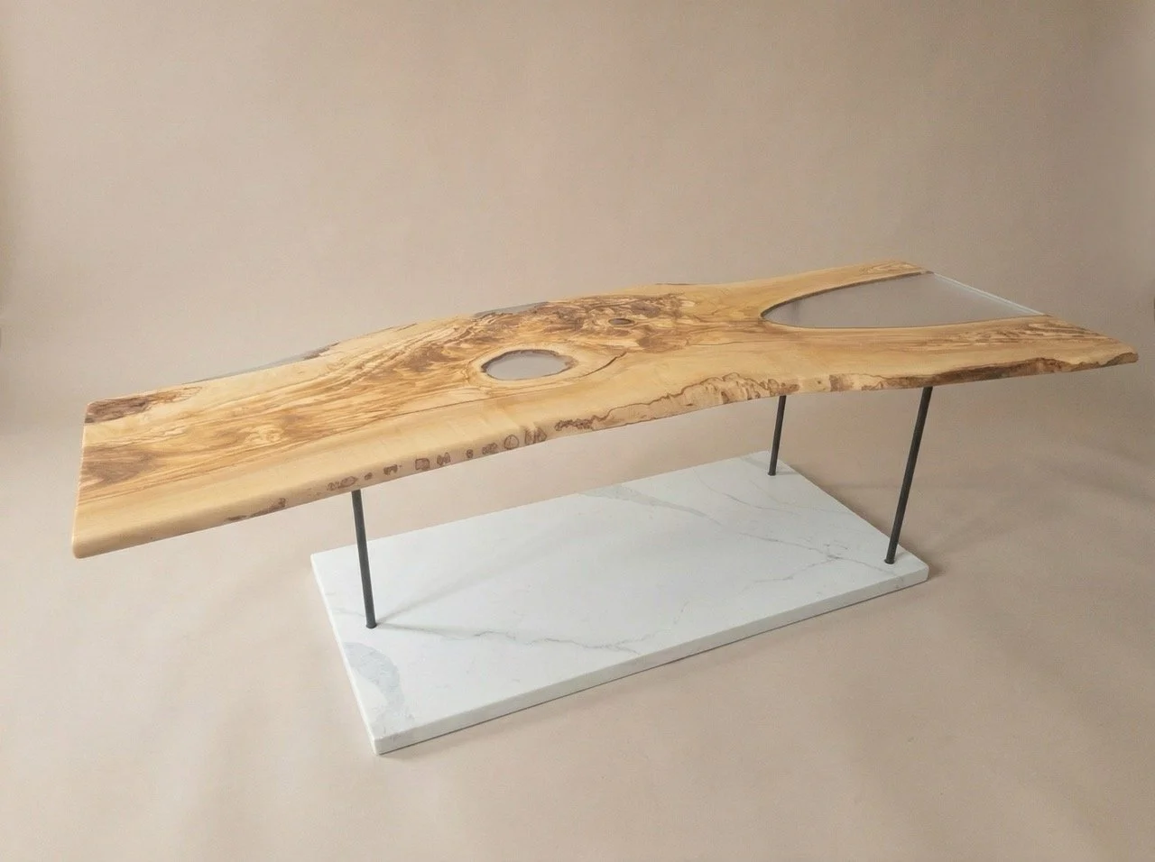 An olivewood table with clear epoxy filling the voids and a white quartz base connected with black steel rods