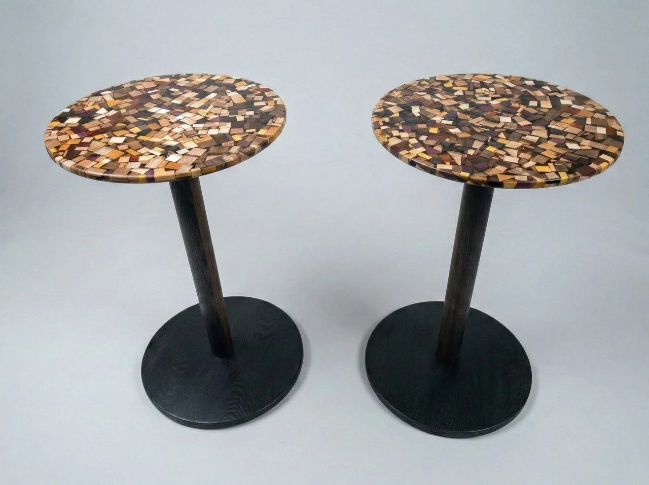Round wooden end tables with black bottoms and posts and tops made of pieces of different species of wood encased in epoxy
