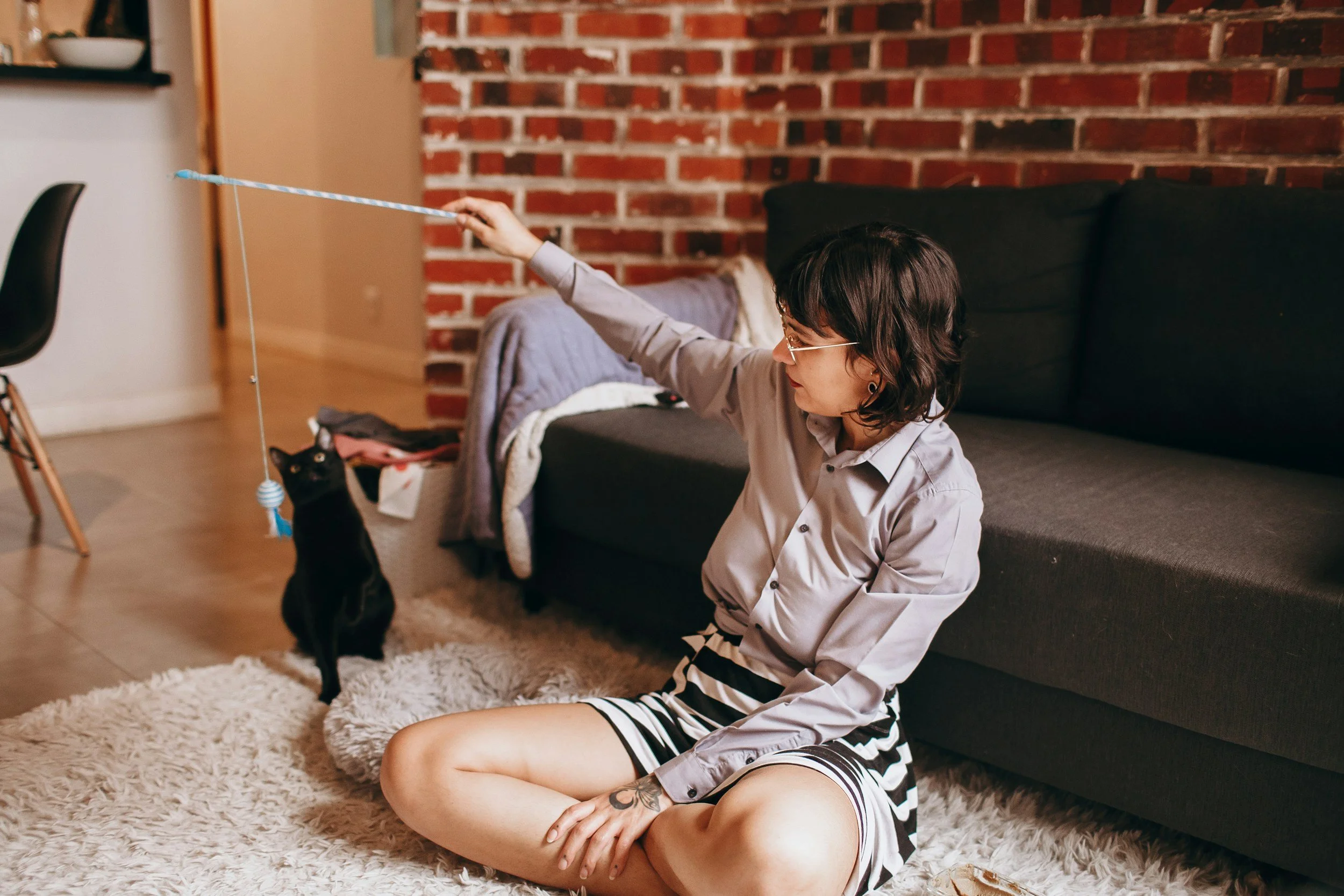a woman in professional clothes sit on the ground and plays with a black cat
