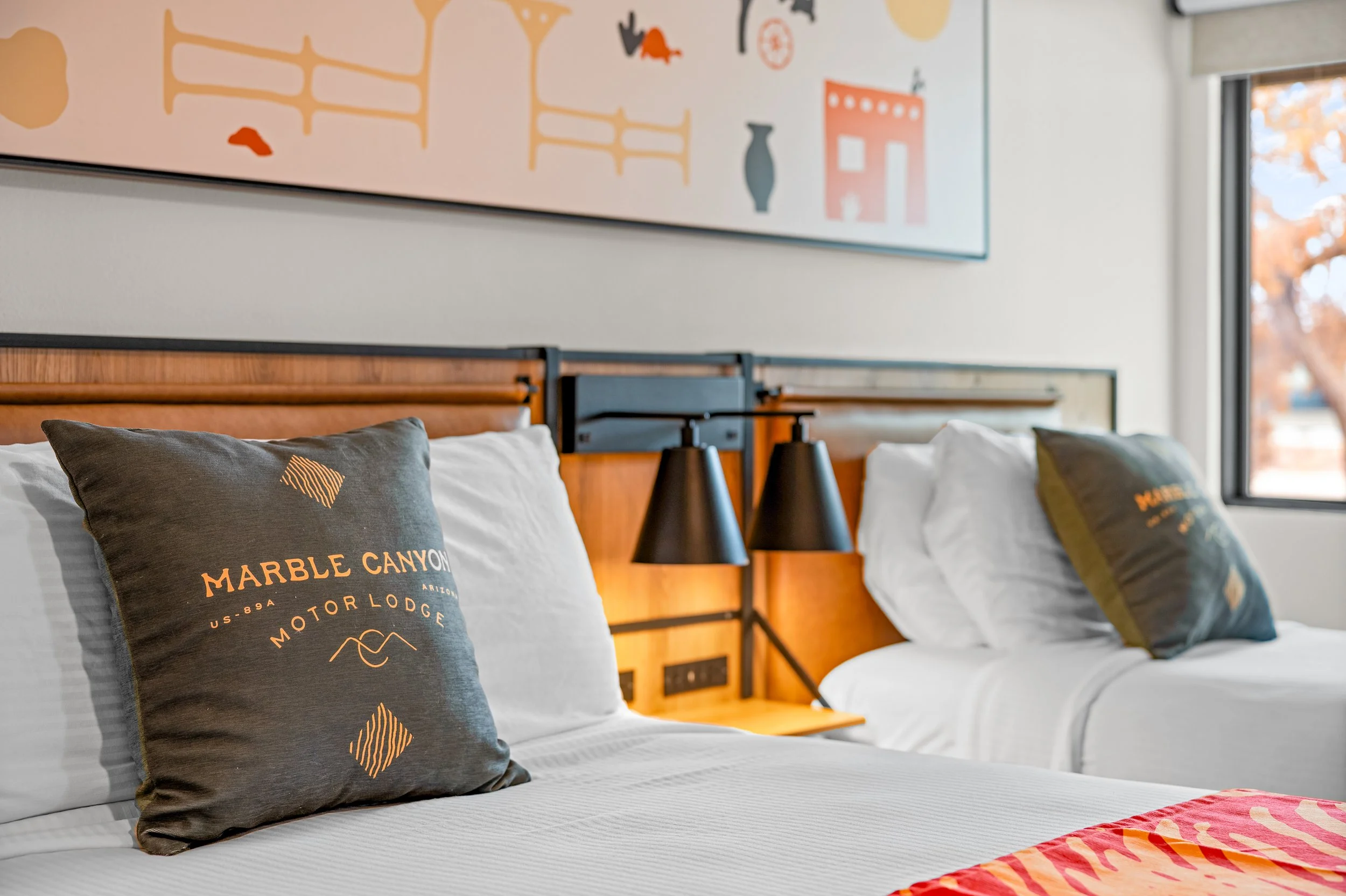 Two neatly made beds with white linens and pillows, each with a black pillow featuring the