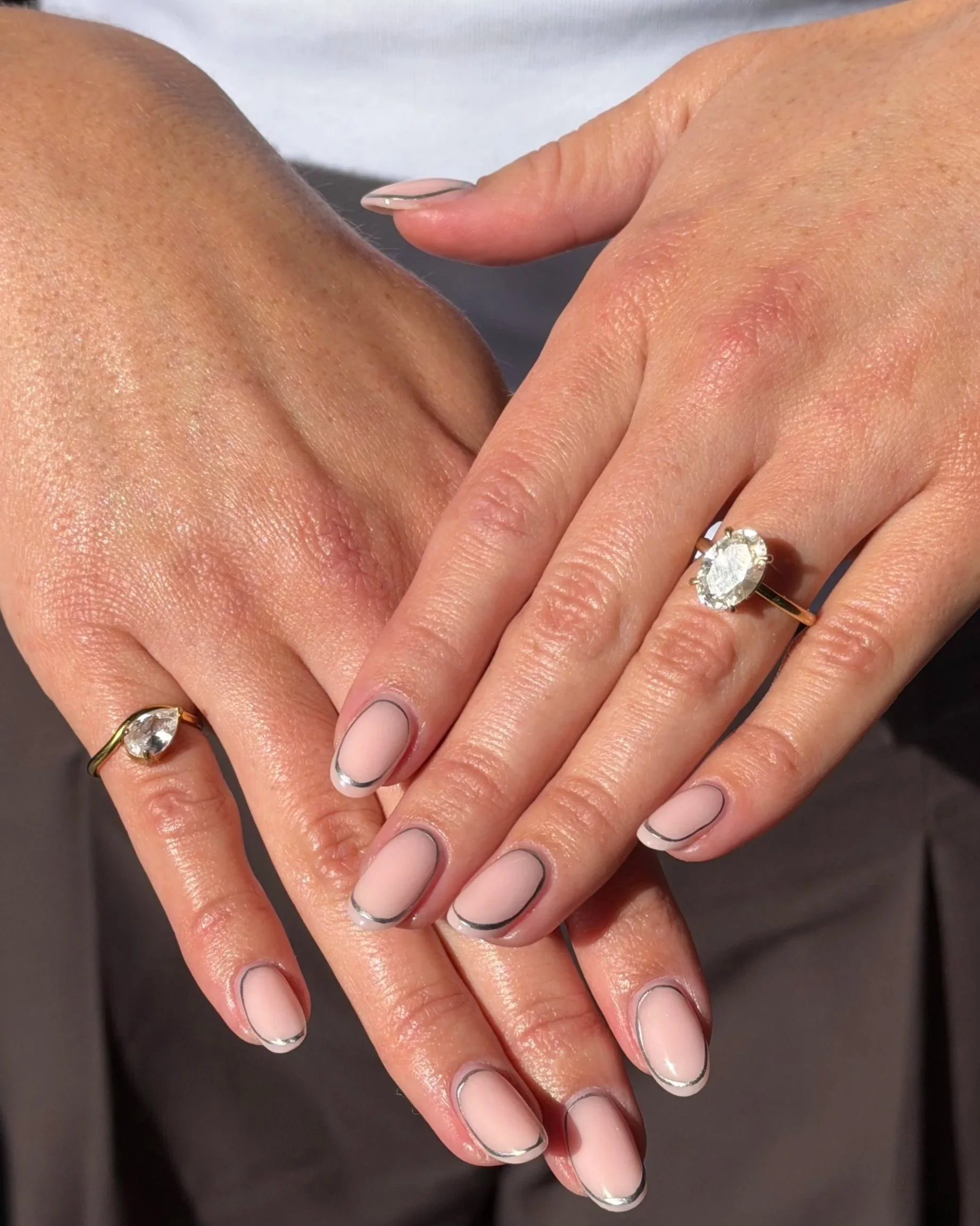Close-up of two hands with neatly manicured nails wearing rings, with a black and white nail design and smooth skin.