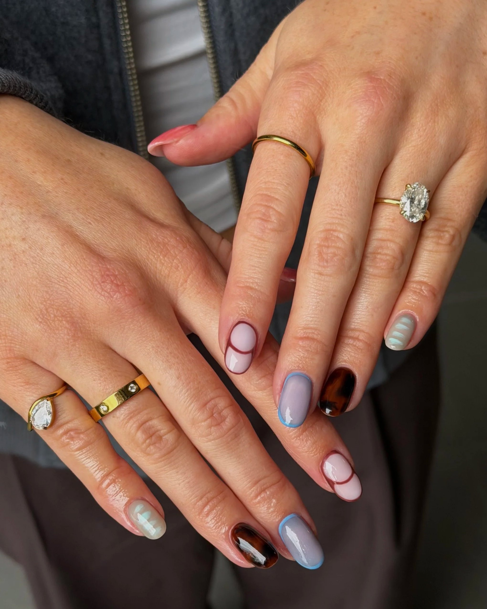 Close-up of hands with multiple rings and decorated nails, resting on a dark surface.