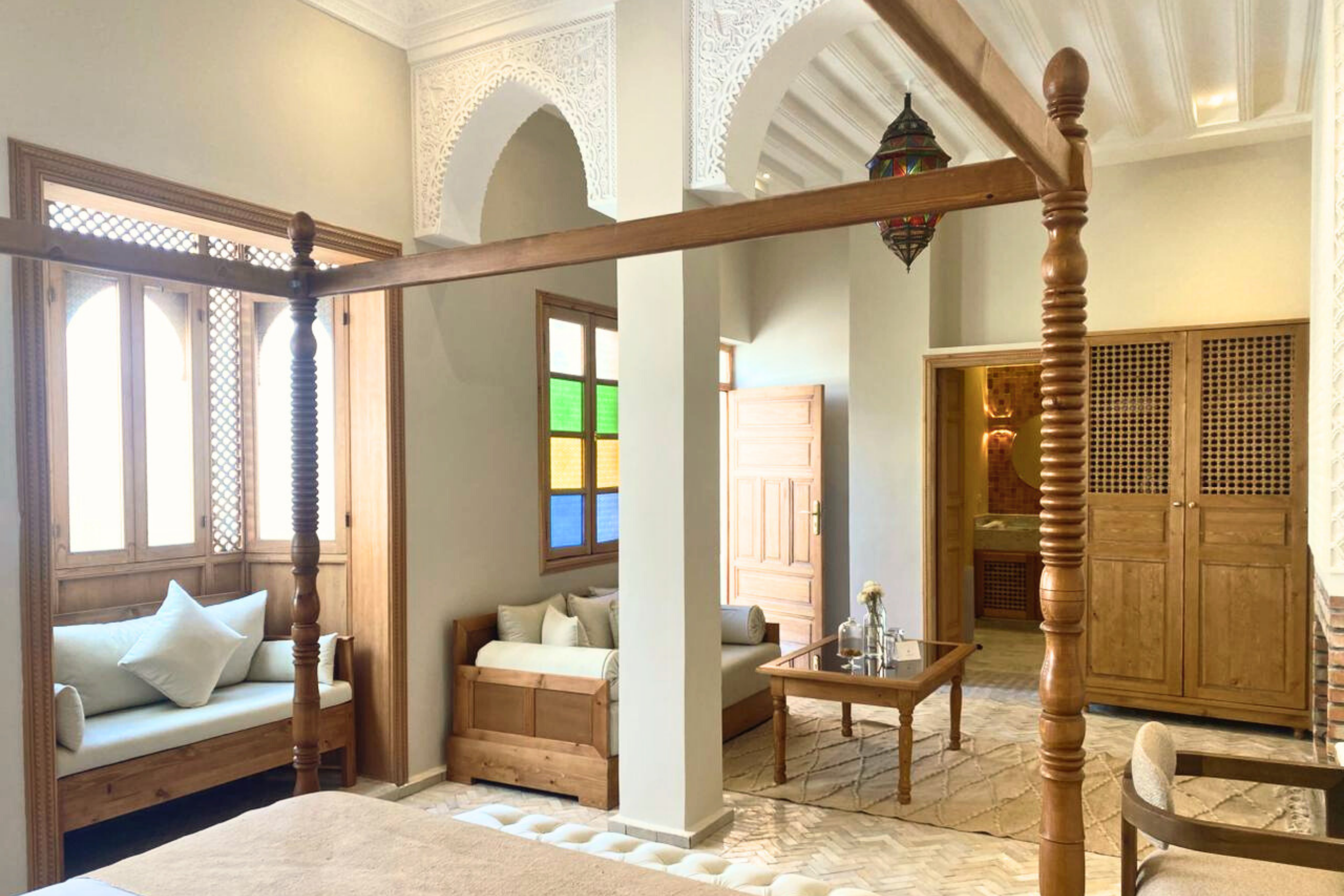 Luxury bathroom with a gold sink, gold faucet, and a large round mirror. There are two bottles of soap or lotion on the sink. Towels are rolled on the countertop. Bathrobes hang on hooks on the wall, and a towel is hanging on a rack. A partial view of a tiled shower with blue and beige mosaic tiles is visible in the background.