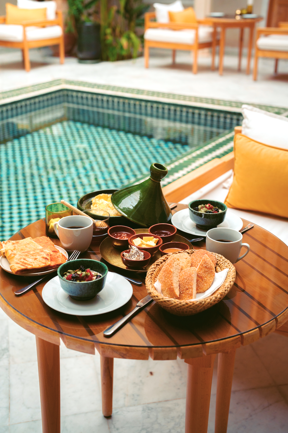 A bedroom with deep red walls and a bed with white and red bedding. There are two gold-colored wall lamps above the head of the bed. A window with colorful stained-glass panes is on the left, and a wooden door frame is partially visible.