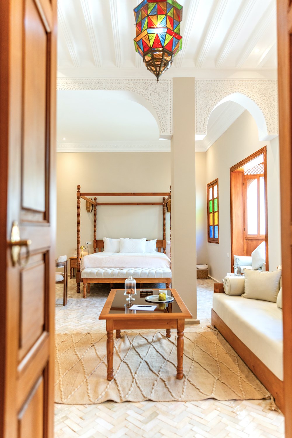 Luxury bathroom with a gold sink, gold faucet, and a large round mirror. There are two bottles of soap or lotion on the sink. Towels are rolled on the countertop. Bathrobes hang on hooks on the wall, and a towel is hanging on a rack. A partial view of a tiled shower with blue and beige mosaic tiles is visible in the background.
