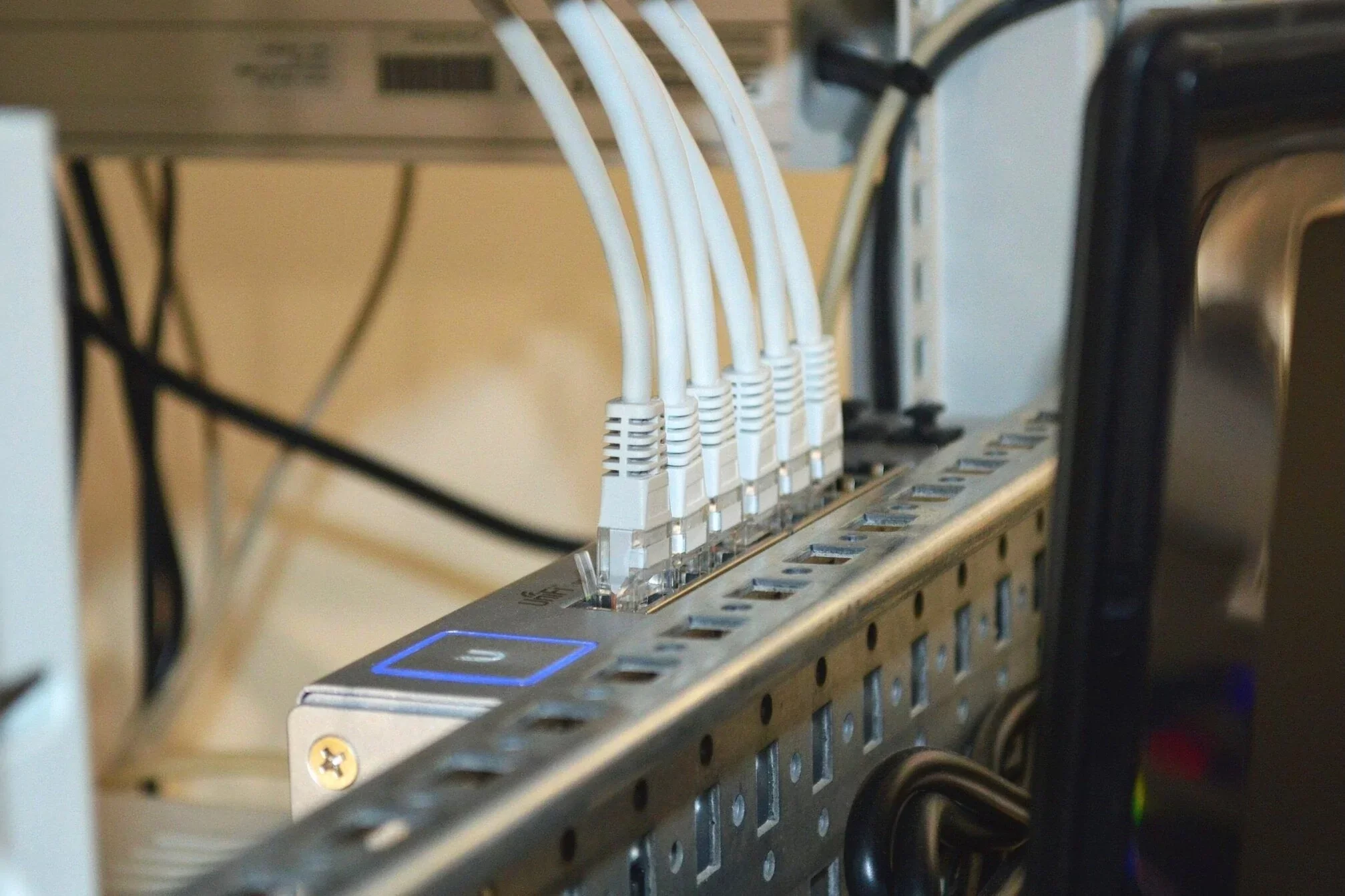 A network switch with several white Ethernet cables plugged into it, mounted on a metal server rack.